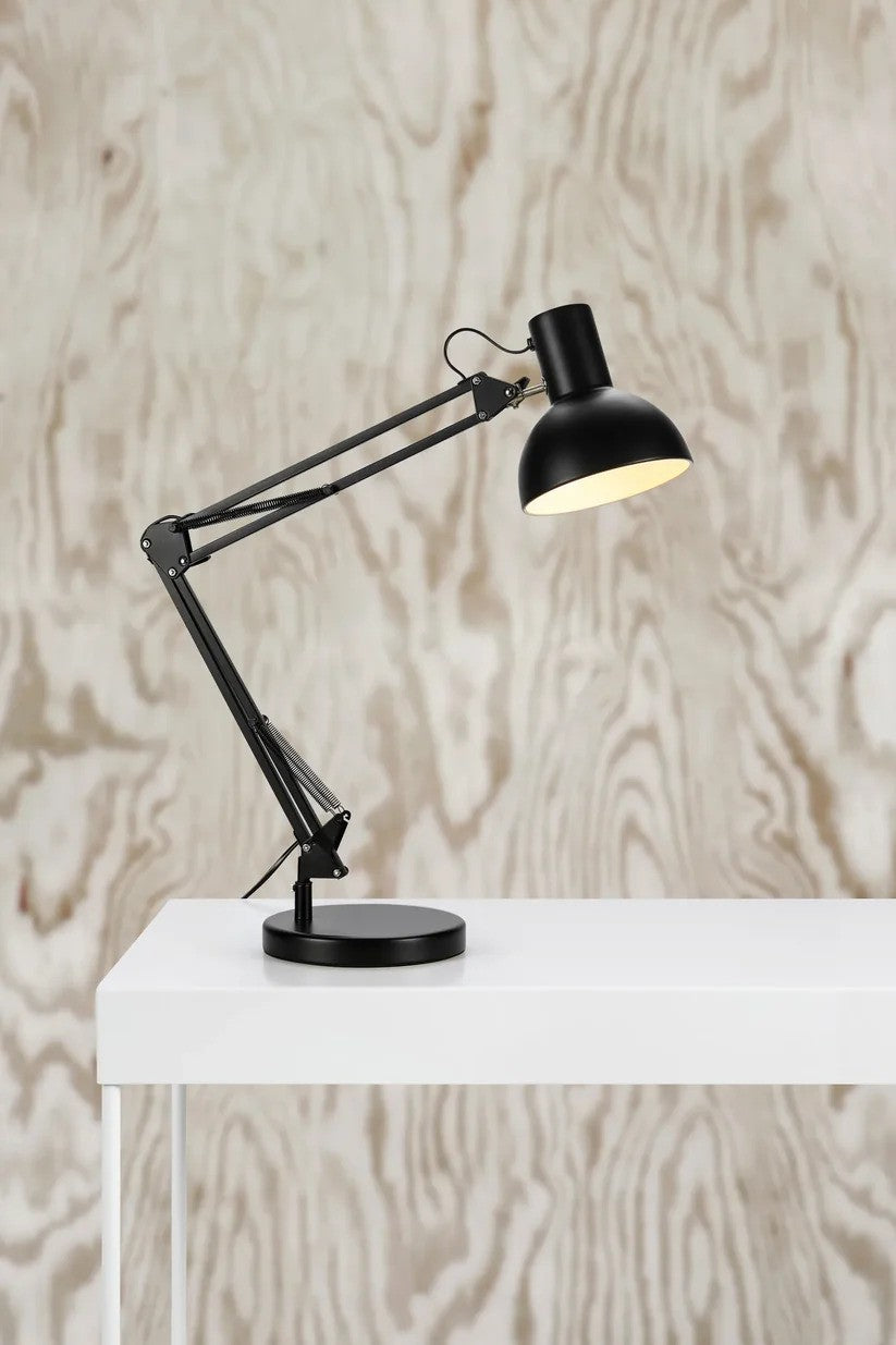 Architect Bordlampe i Sort placeret på et bord med en flot kontrast til væggen