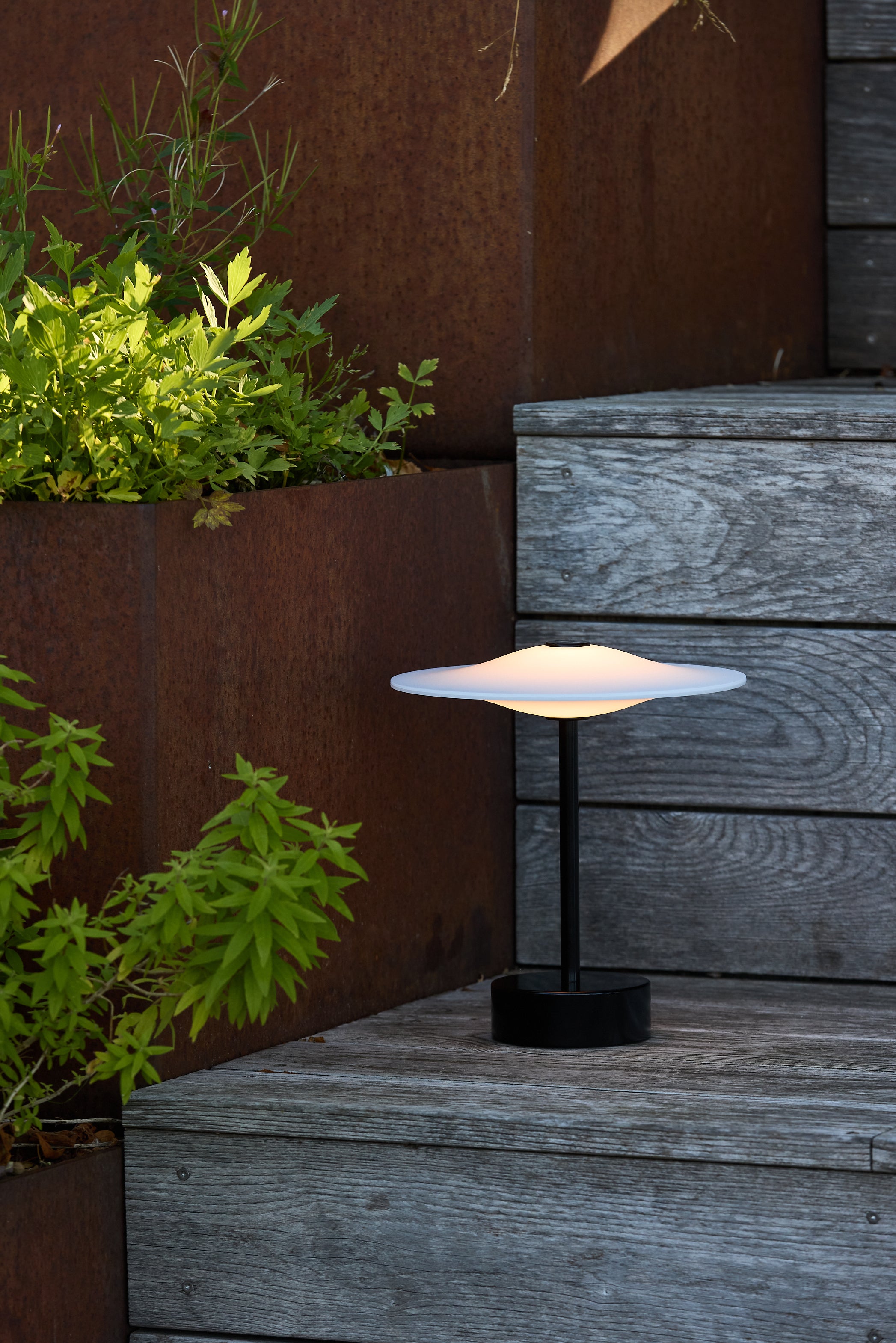 Den unikke designet Piet Hein Sinus22 Bordlampe i Sort placeret udenfor på trappen for dens varme belysning