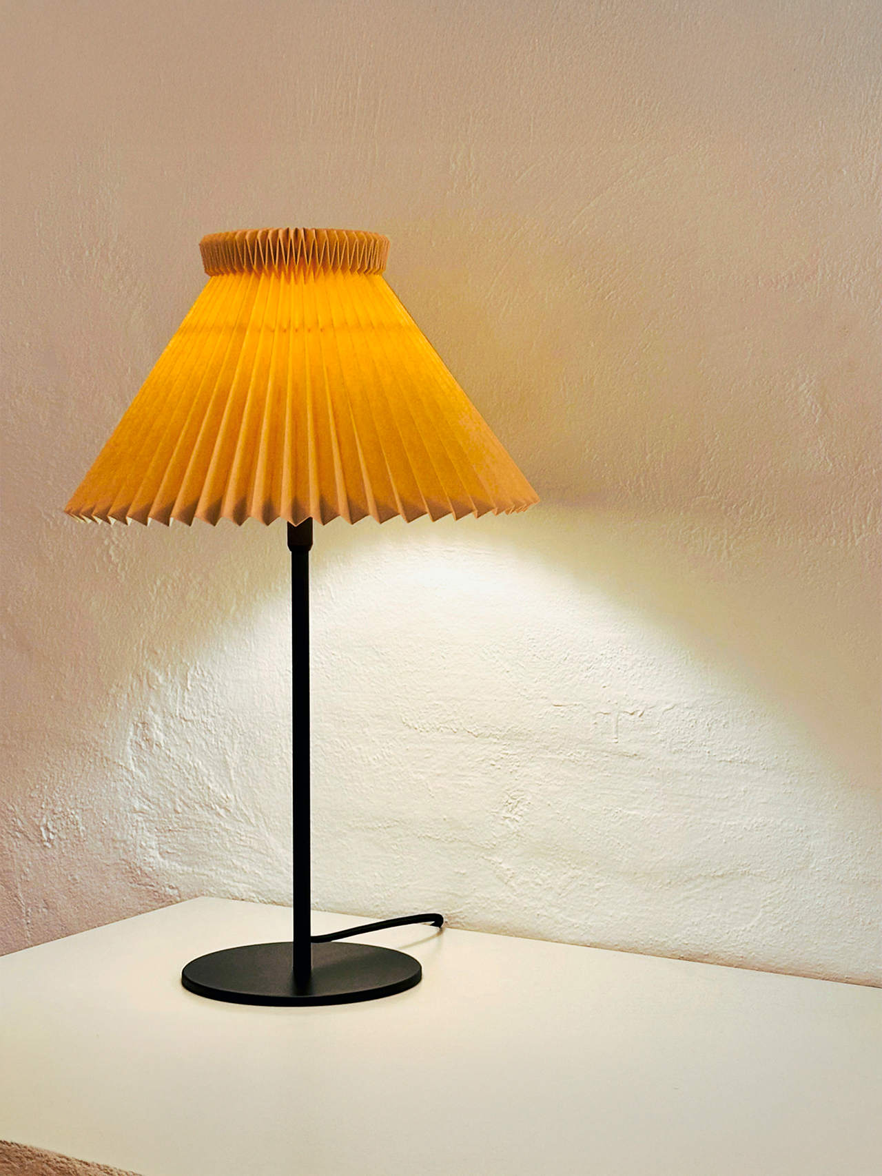 Beige Le Klint 334 bordlampe i kontrast med hvid væg og bordplade