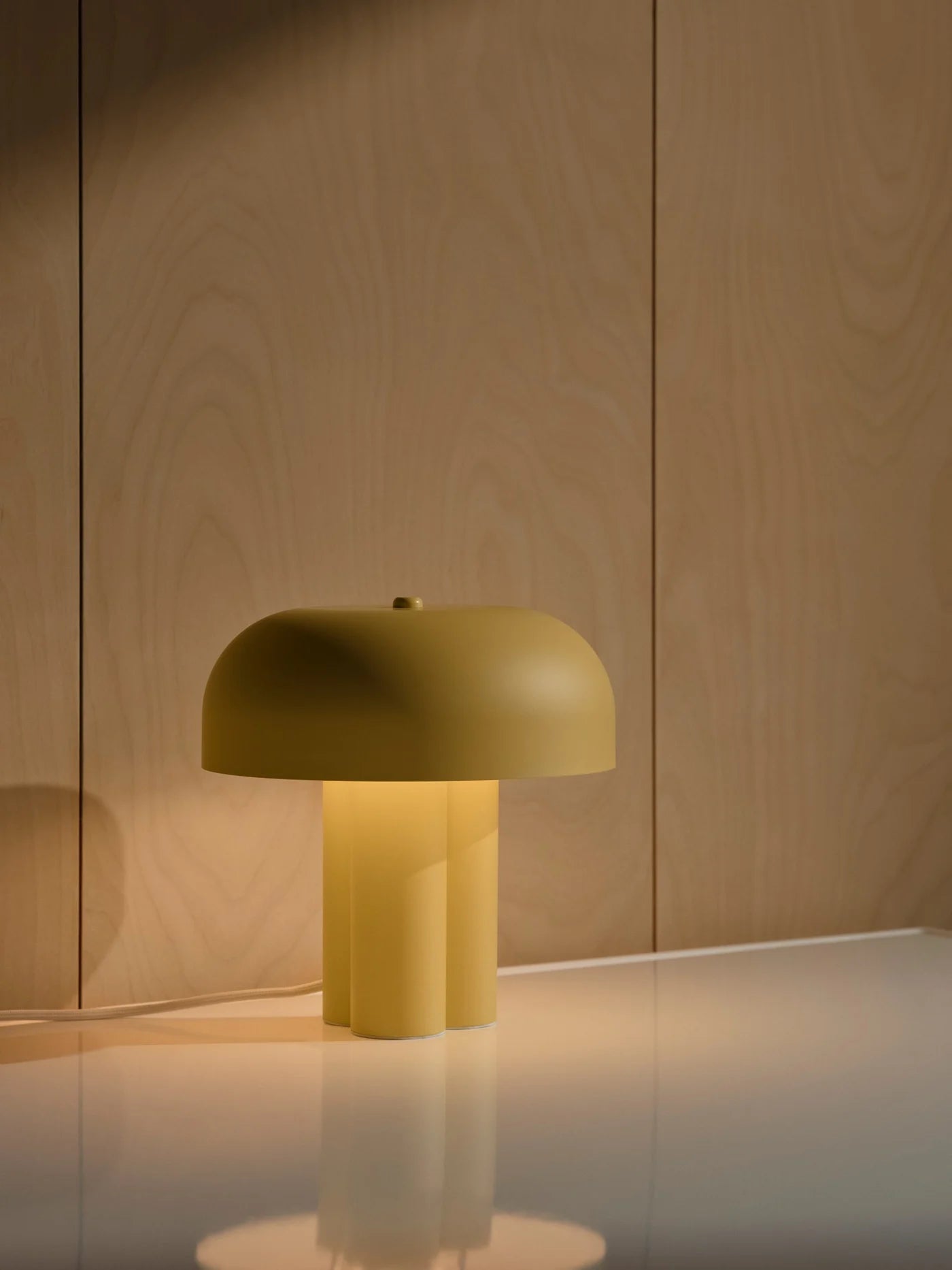 Den unikke designet Sandro Bordlampe i Gul stillet op foran en væg for den flotte kontrast