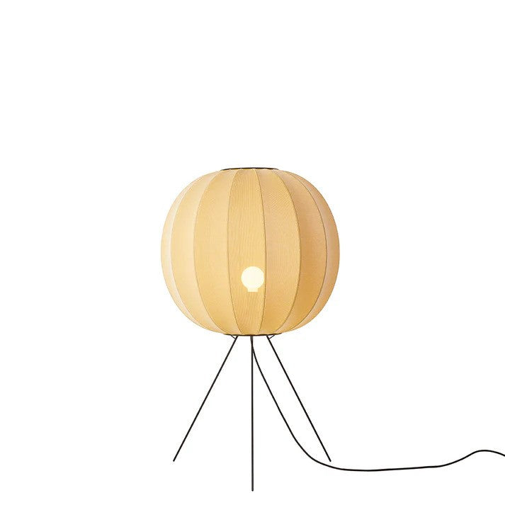 Den unikke designet Knit-Wit Ø60 Round Gulvlampe Medium i Sunrise placeret foran en hvid væg for en flot kontrast med en E27 pære iført og tændt for
