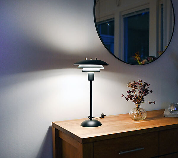 Den unikke designet Epsilon Bordlampe i Sort placeret på skuffen i stuen for dens flotte og behagelige belysning