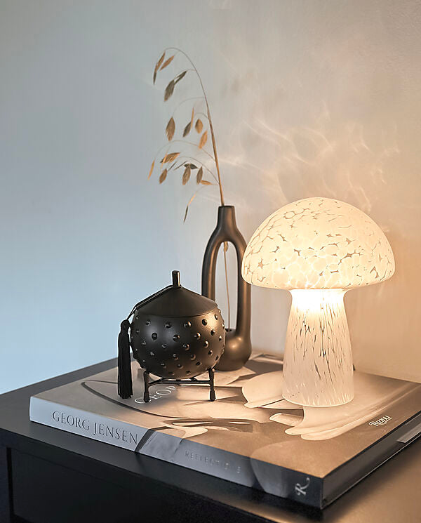 Den unikke designet Mushi lille Bordlampe i Hvid placeret i stuen med tændt lys for dens behagelige belysning