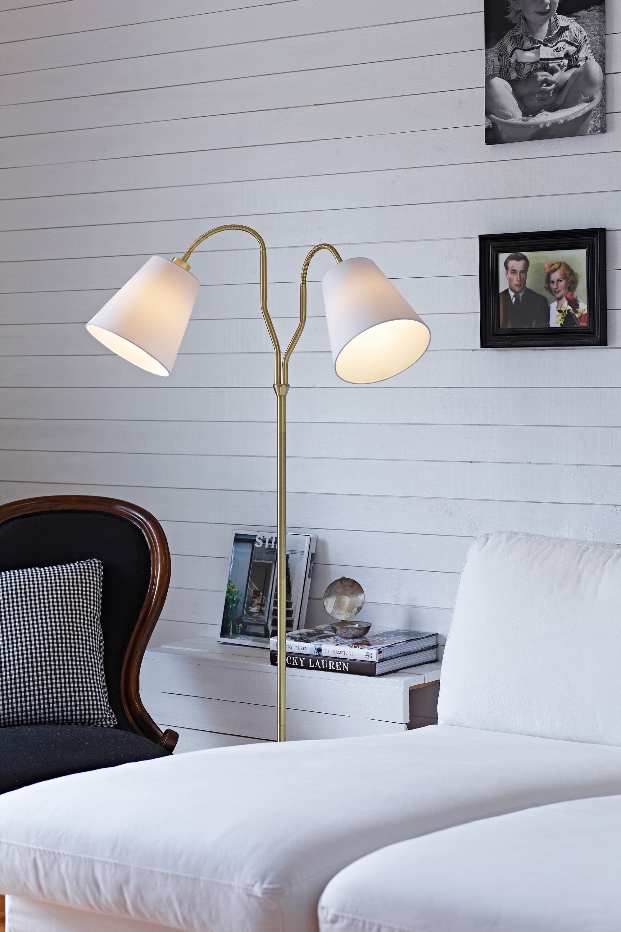 Den elegante gulvlampe fra Markslöjd Modena Gulvlampe i Messing/Hvid placeret i hjørnet af stuen ved siden af sofaen