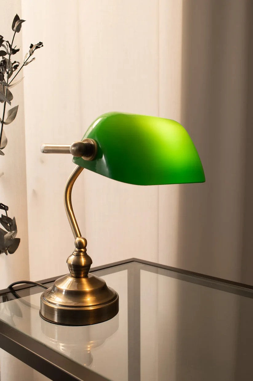 Bankers Bordlampe i Grøn 25 cm placeret på et glasbord i stuen for det elegante look og hyggelige lys