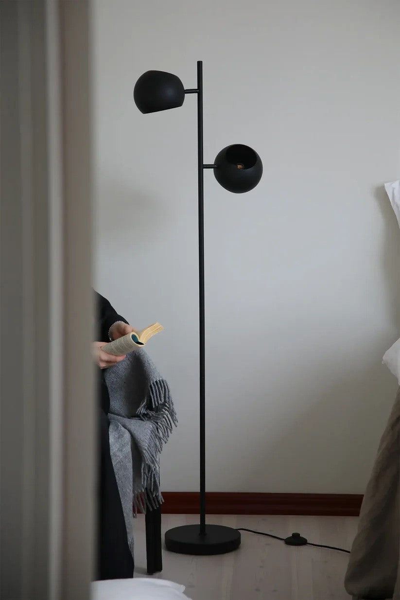 Edgar Gulvlampe 2L i Sort stillet ved siden af læsestolen for det behagelig lys og elegante udseende