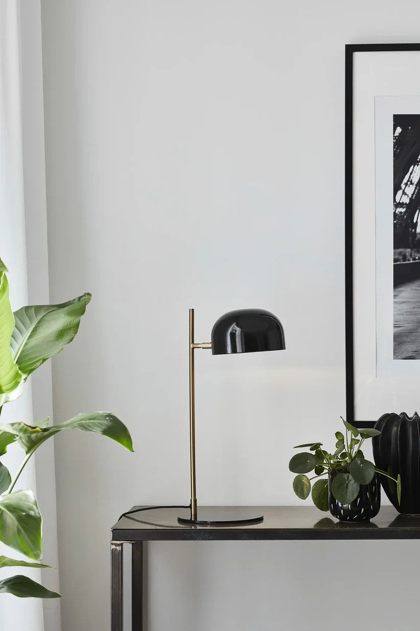 Den æstetiske skrivebordslampe fra Markslöjd Pose Bordlampe i Sort/Messing placeret på hylden