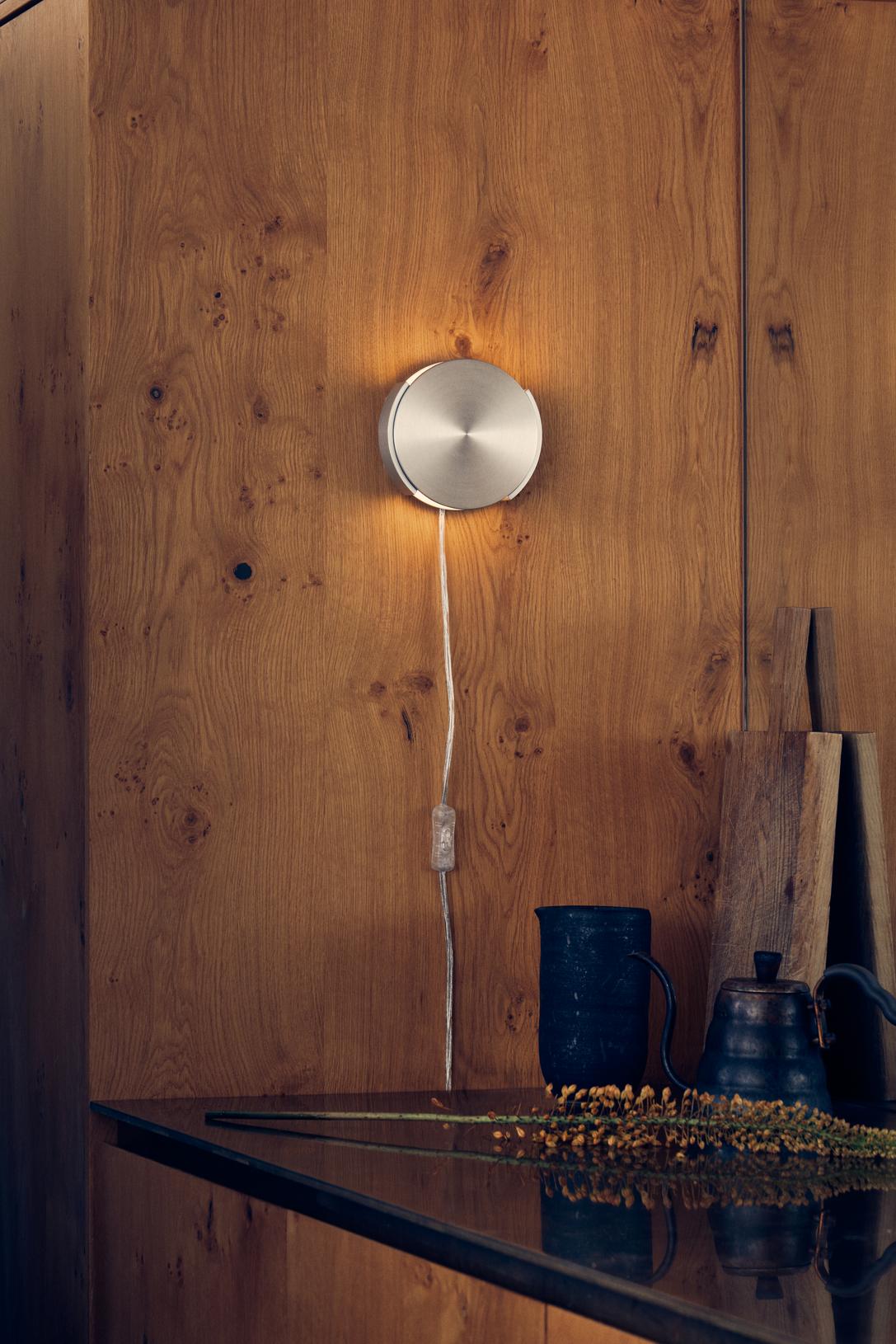 Frandsens Rotate Wal Lamp i Brushed Aluminium hængt op på væggen ved siden af bordet