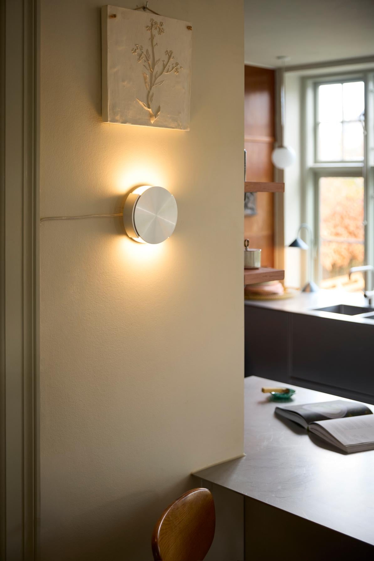 Frandsens Rotate Wall Ø15 Børstet Aluminium tændt og hængt op på væggen i stuen
