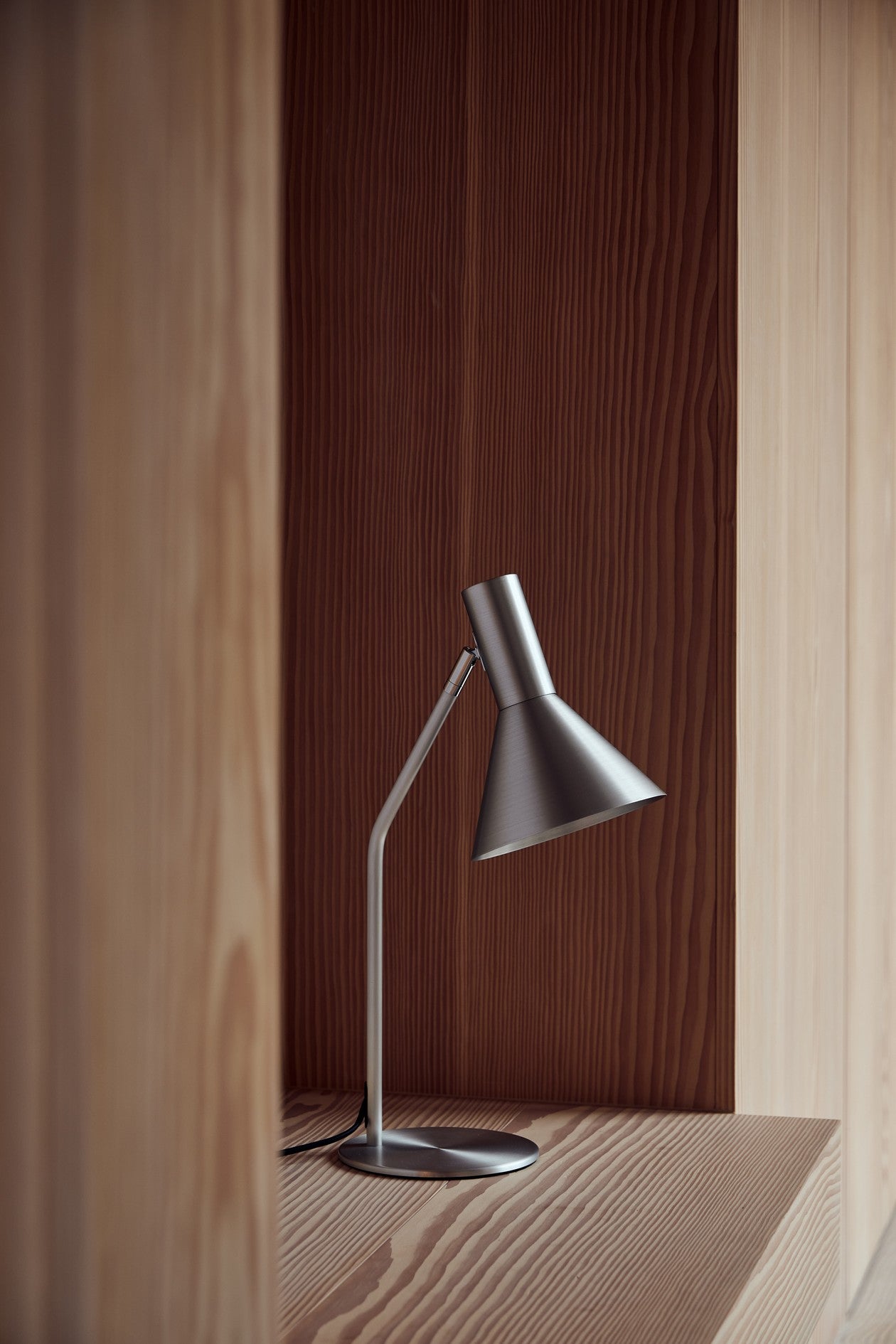 Den æstetiske Lyss Bordlampe i Brushed Aluminium placeret på hylden i stuen for dens behagelige belysning og elegante design