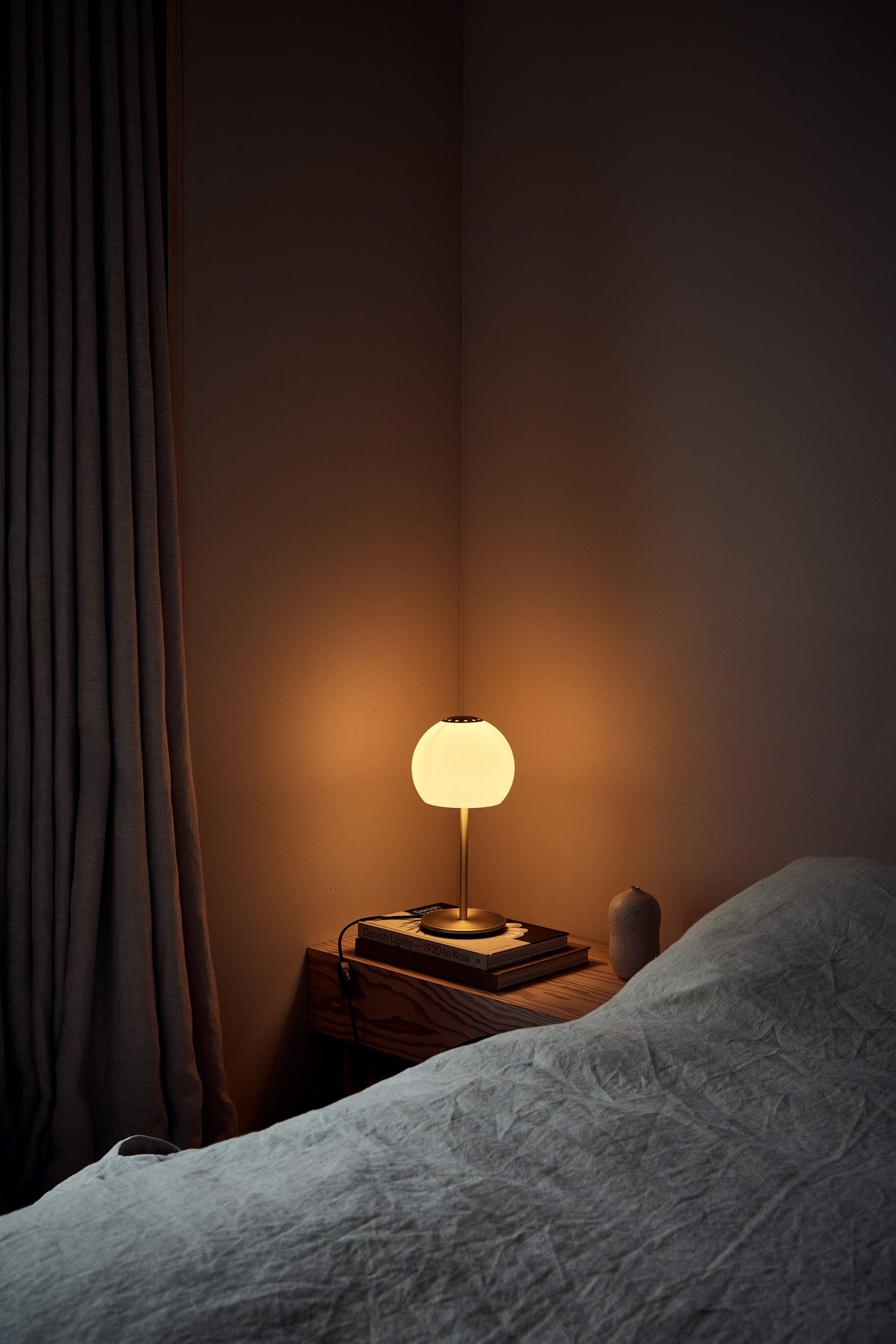Den æstetiske Ball Glass Bordlampe Ø18 i Sandgrå placeret på sengebordet for dens behagelige belysning og unikke design