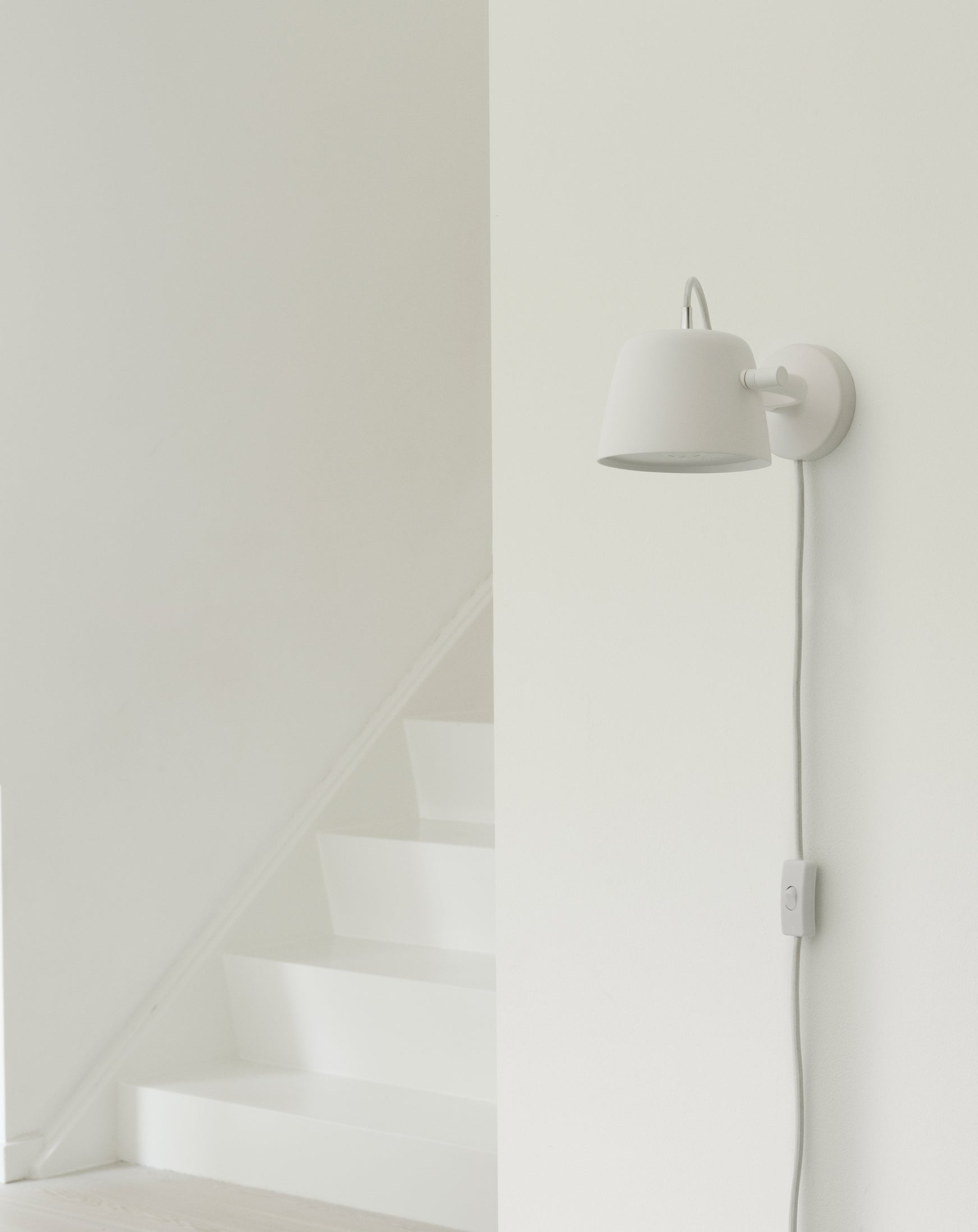 Hvid væglampe fra Normann Copenhagen ved en trappe