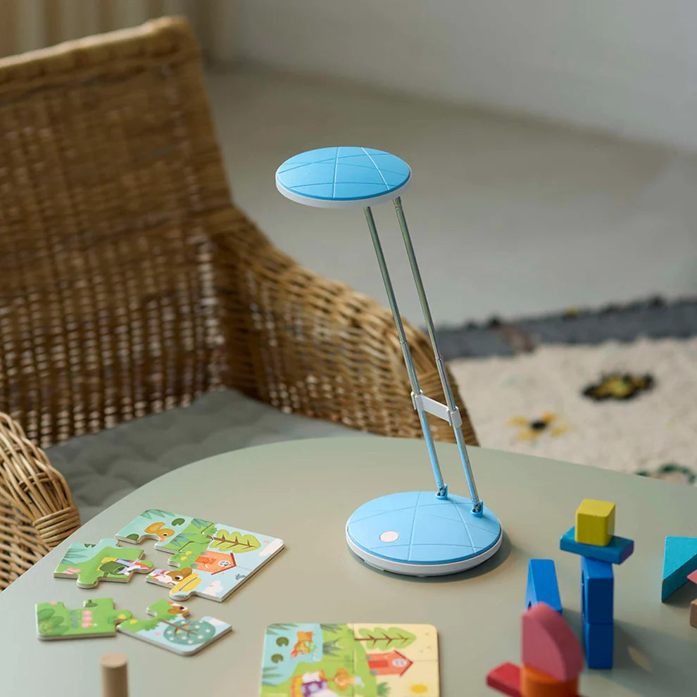 Den æstetiske A5 LED Bordlampe i Lyseblå placeret på et bord i stuen for dens varme belysning