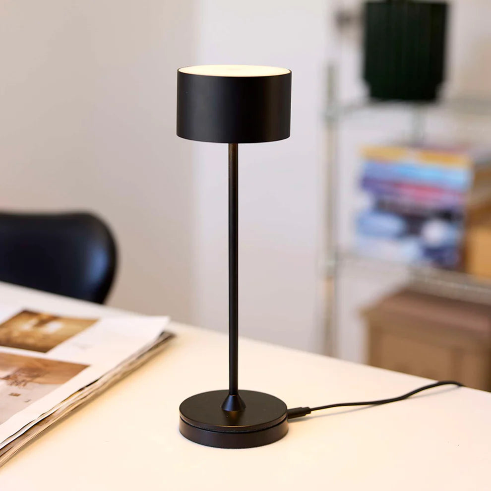 Den æstetiske Bistro LED Bordlampe i Sort placeret i sin lade station på et bord i stuen