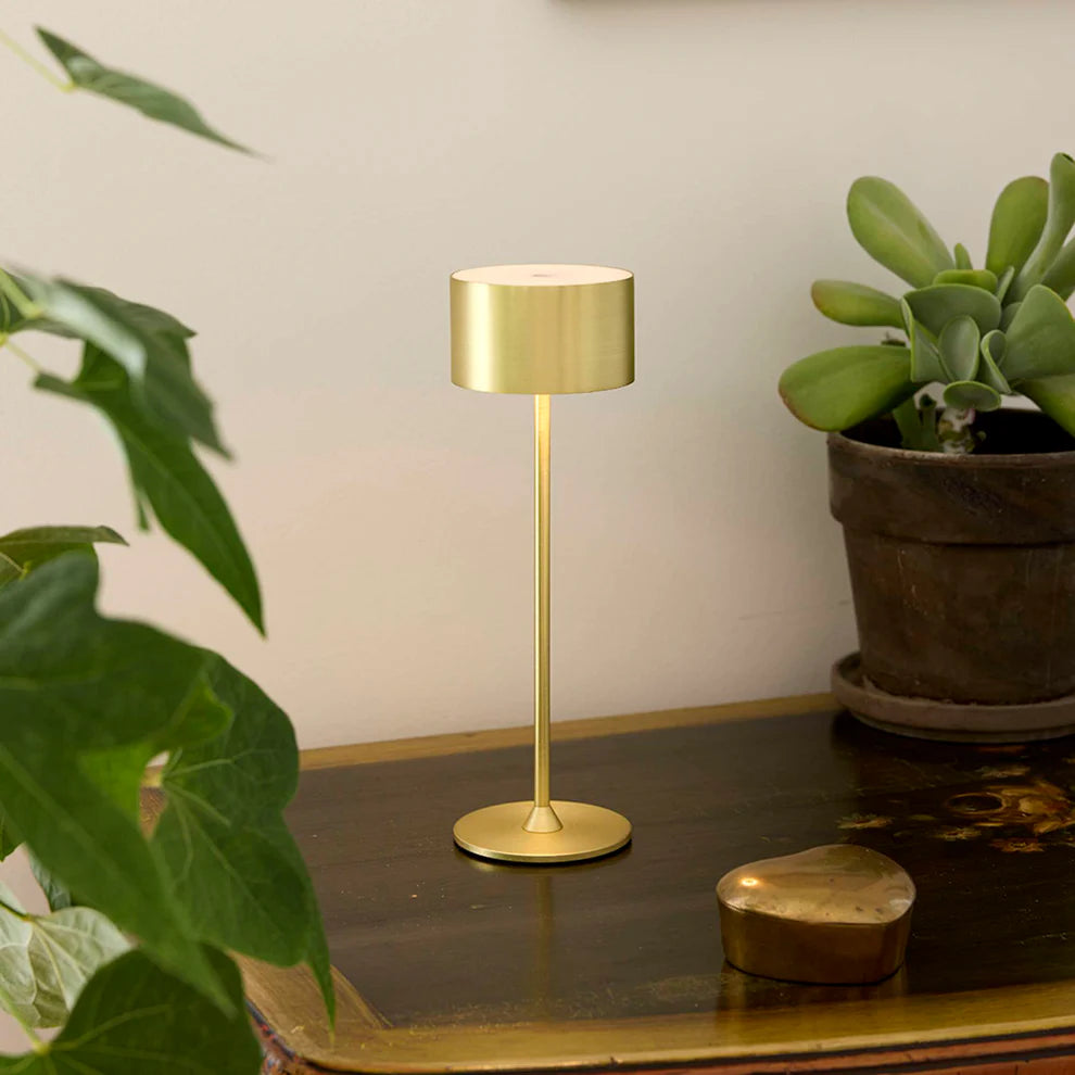 Den æstetiske Bistro LED Bordlampe i Børstet Messing placeret i stuen for dens varme belysning