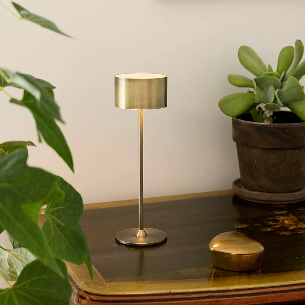 Den æstetiske Bistro LED Bordlampe i Antik Børstet Messing placeret i stuen for dens behagelige belysning