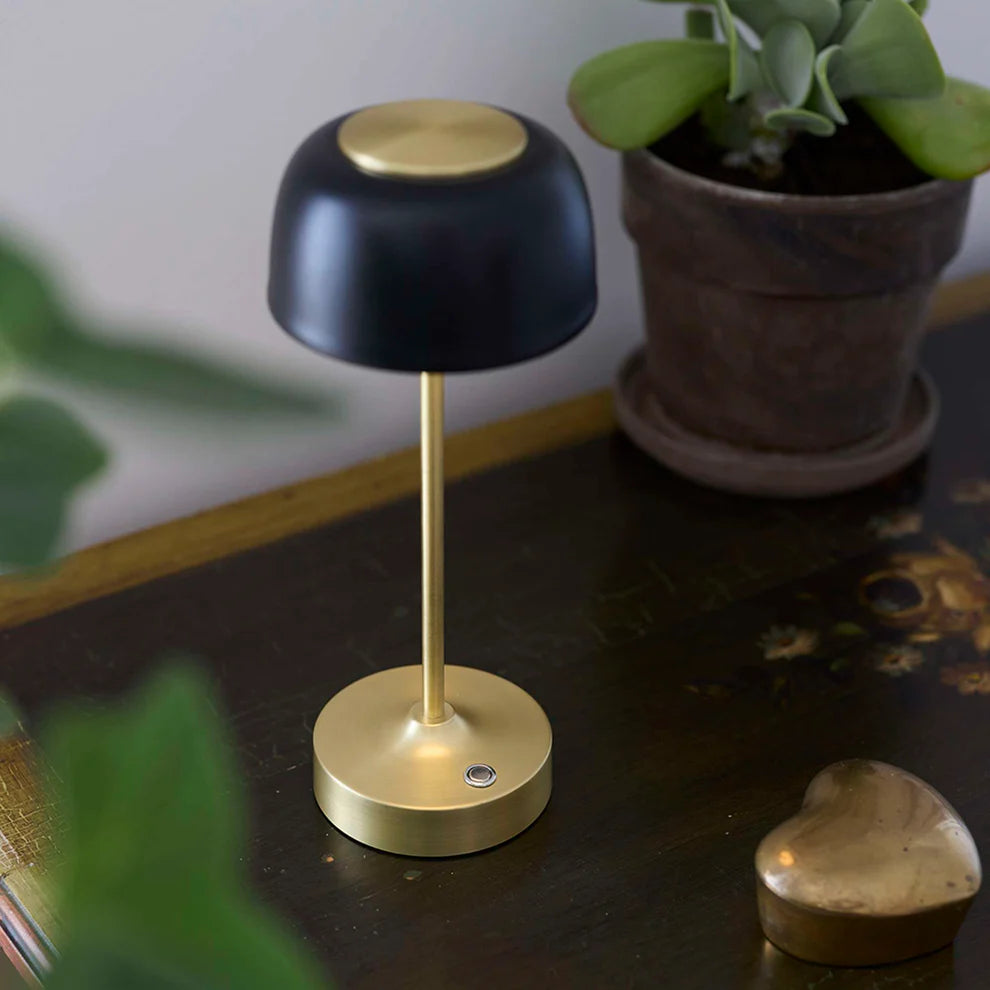 Den æstetiske Royal LED Bordlampe i Sort/Guld placeret i hjørnet af stuen for dens varme belysning