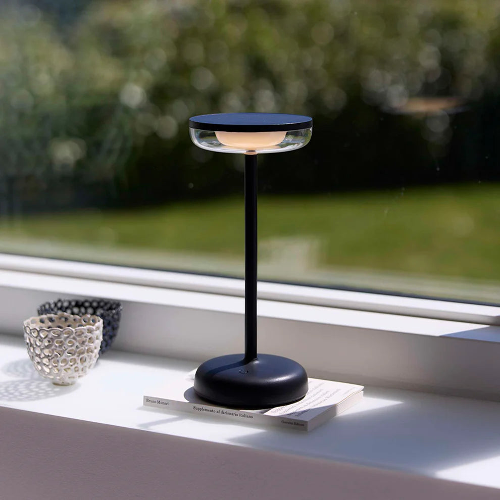 Den æstetiske Breeze LED Bordlampe i Sort placeret i vindueskammen af stuen for dens varme belysning