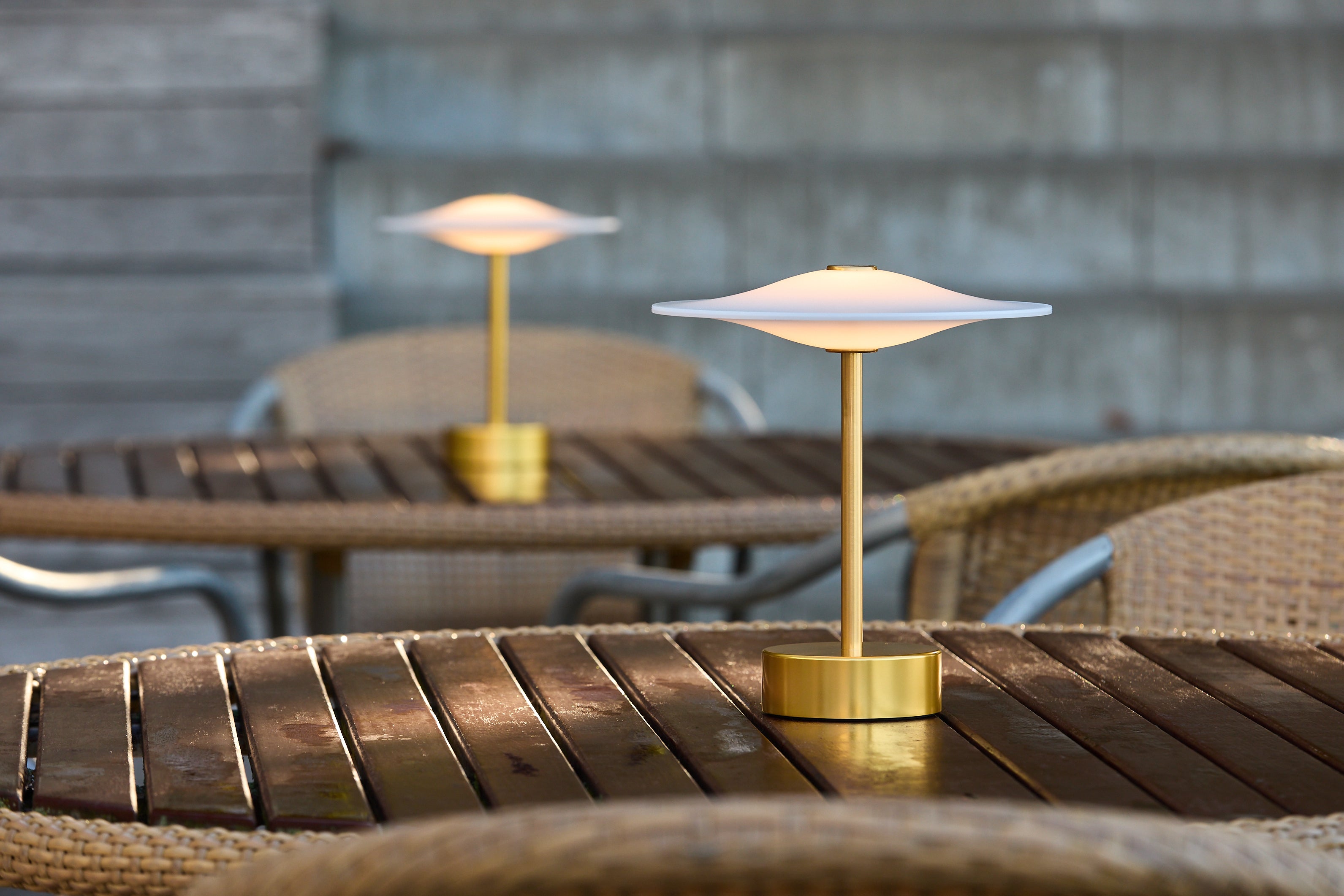 Piet Hein Sinus22 Bordlampe i Messing placeret udenfor på et bord for dens behagelige belysning