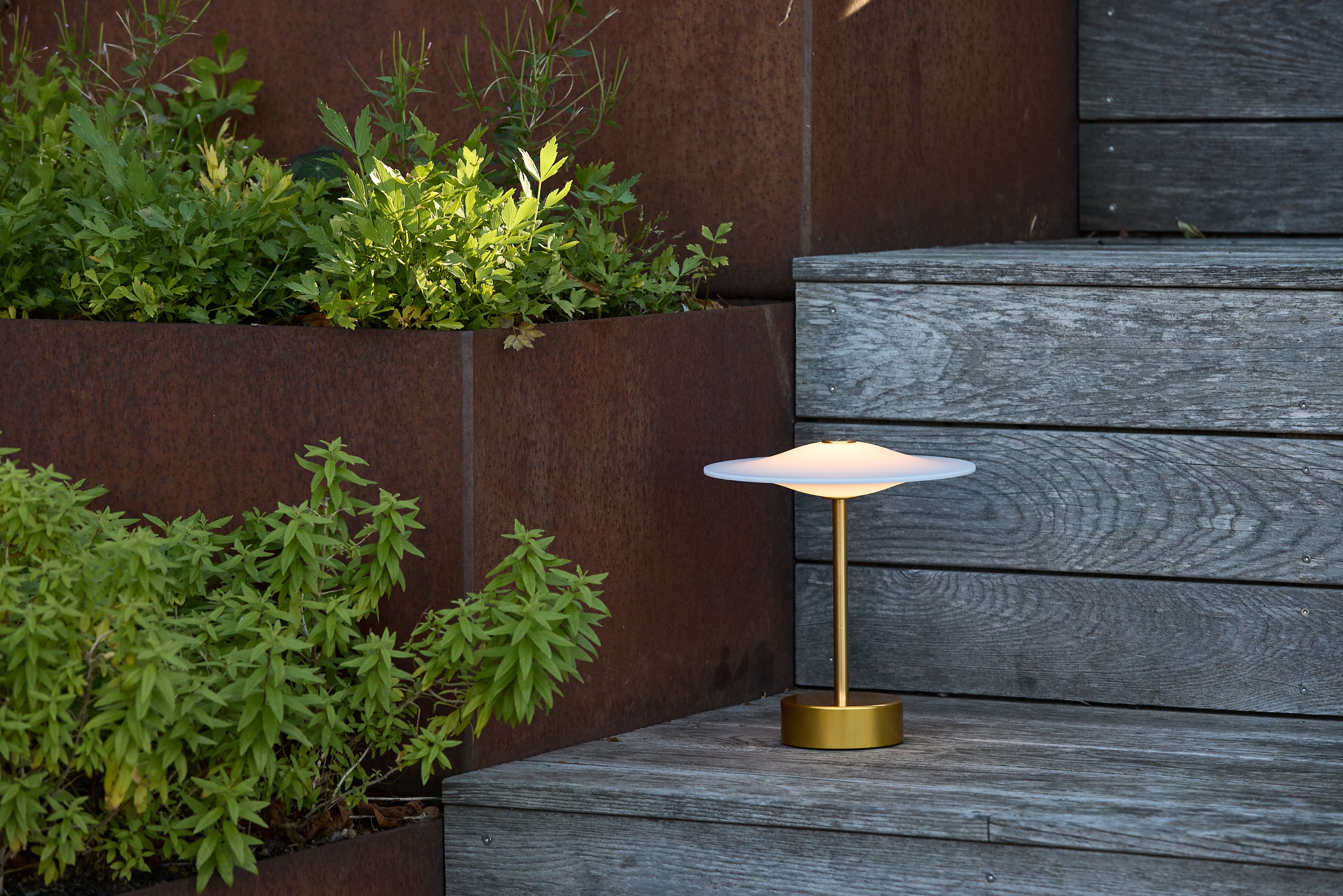 Den elegante Piet Hein Sinus22 Bordlampe i Messing placeret på trapperne udenfor huset