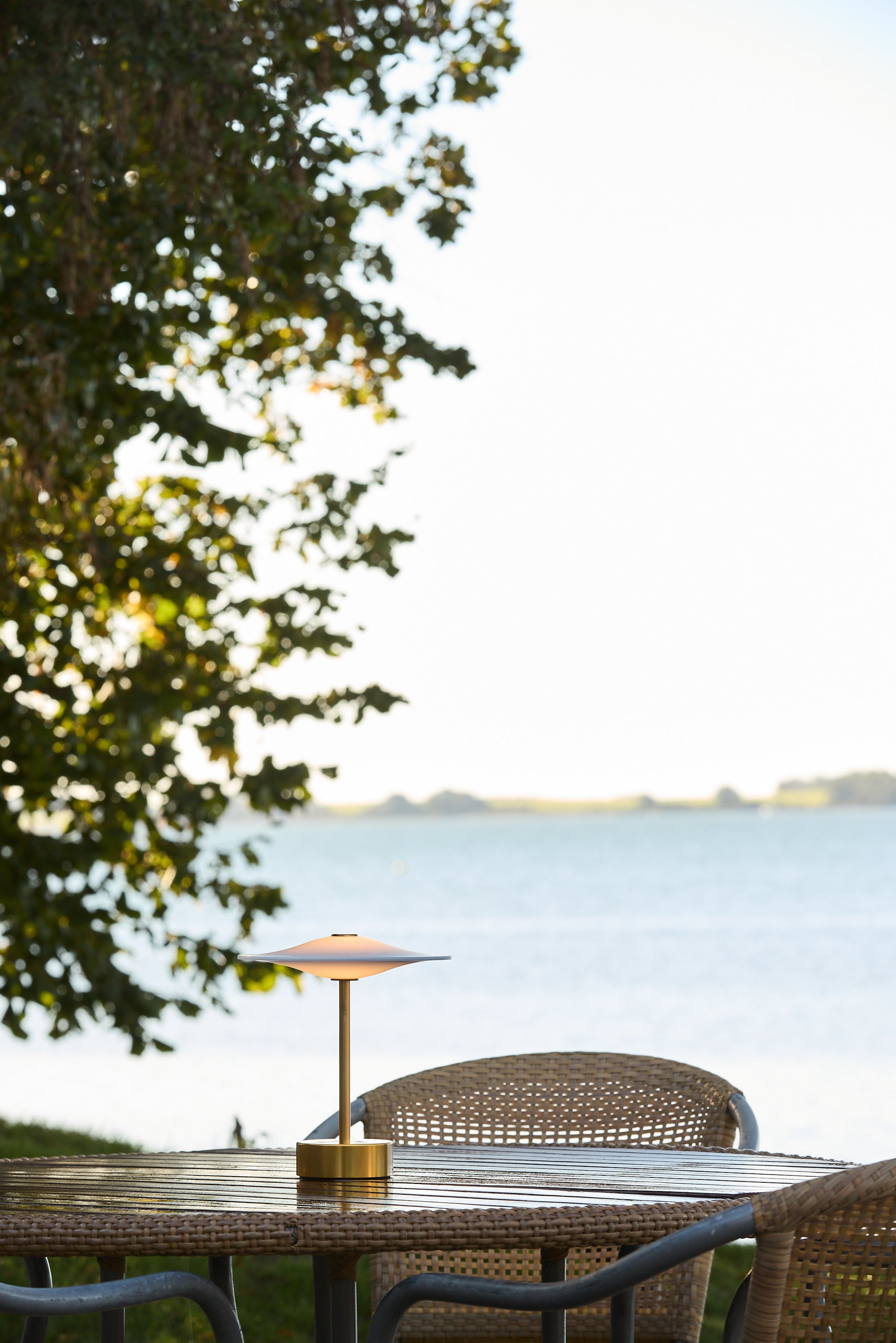 Den æstetiske Piet Hein Sinus22 Bordlampe i Messing placeret udenfor på havebordet for dens hyggelige belysning