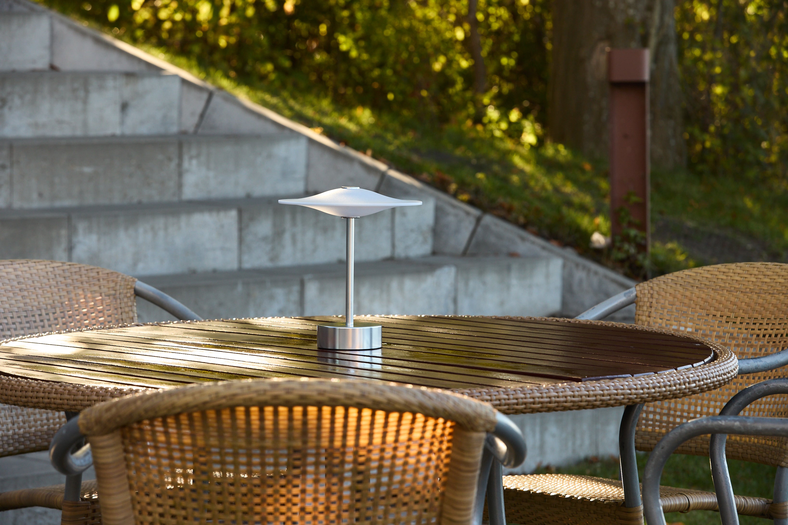 Piet Hein Sinus22 Bordlampe i Stål placeret på havebordet for dens unikke design og varme belysning