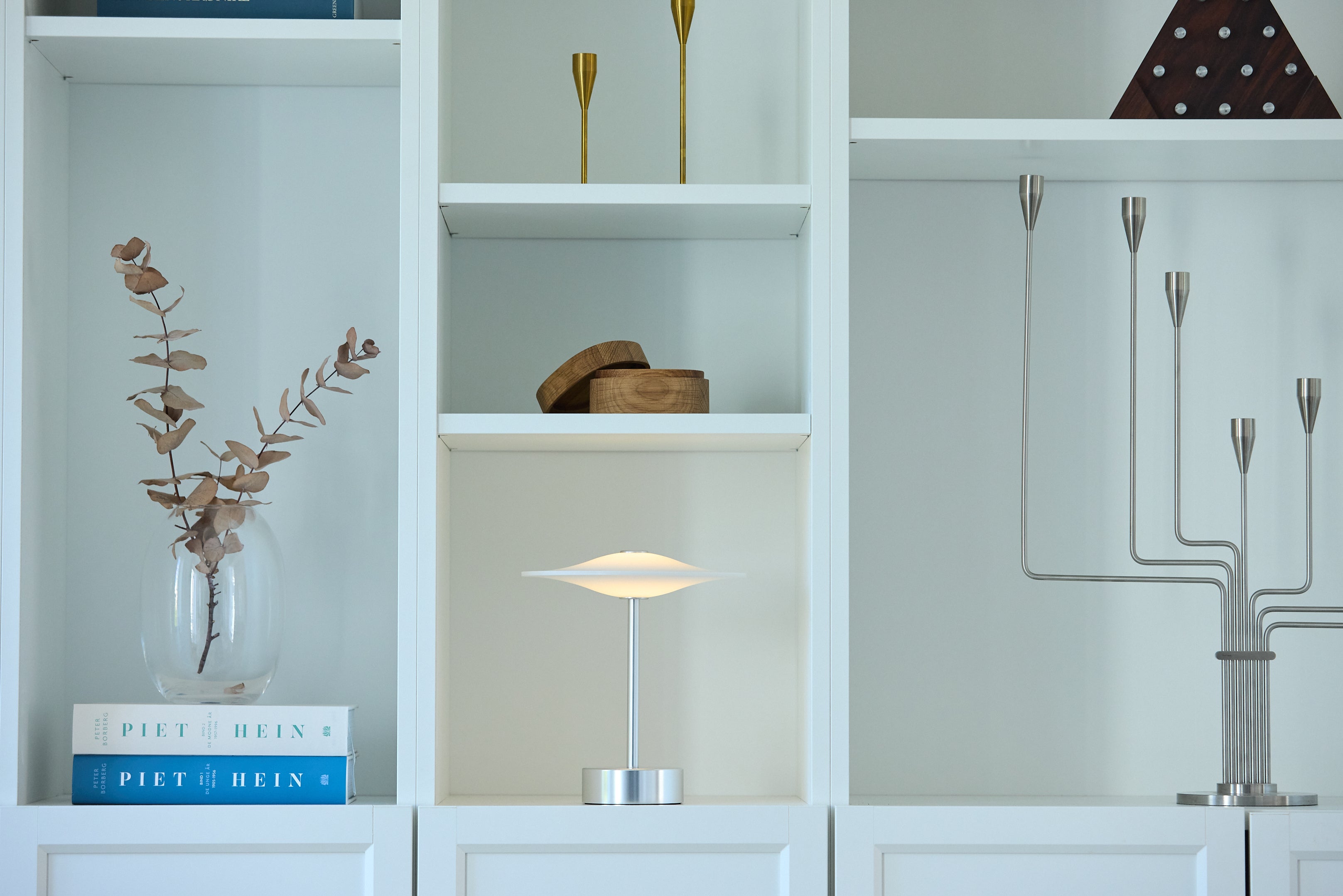 Den æstetiske Piet Hein Sinus22 Bordlampe i Stål placeret på hylden i stuen for dens behagelige belysning