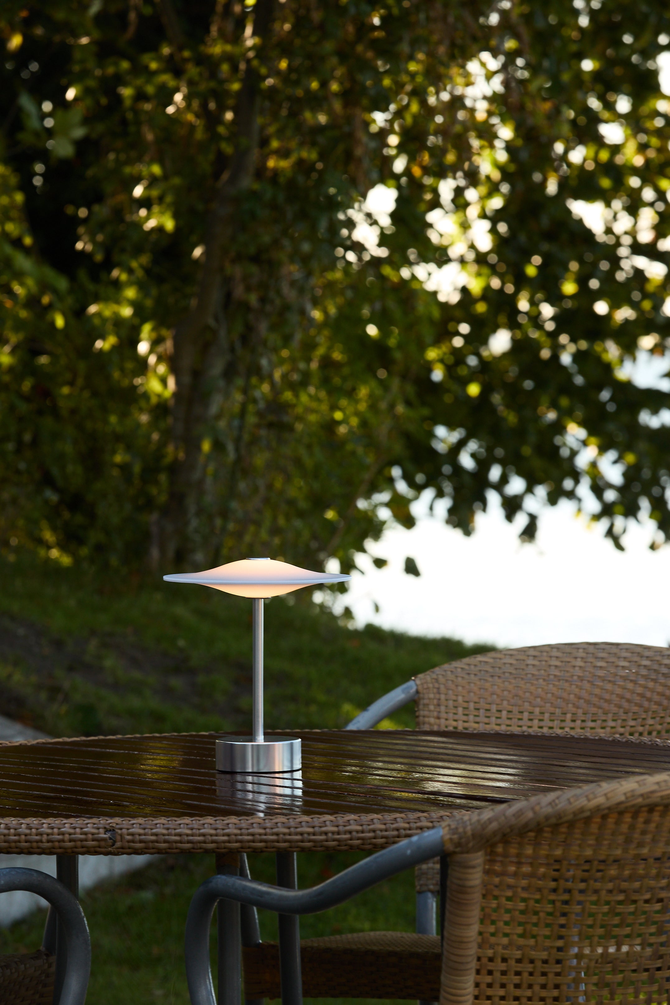 Den unikke designet Piet Hein Sinus22 Bordlampe i Stål placeret udenfor på havebordet