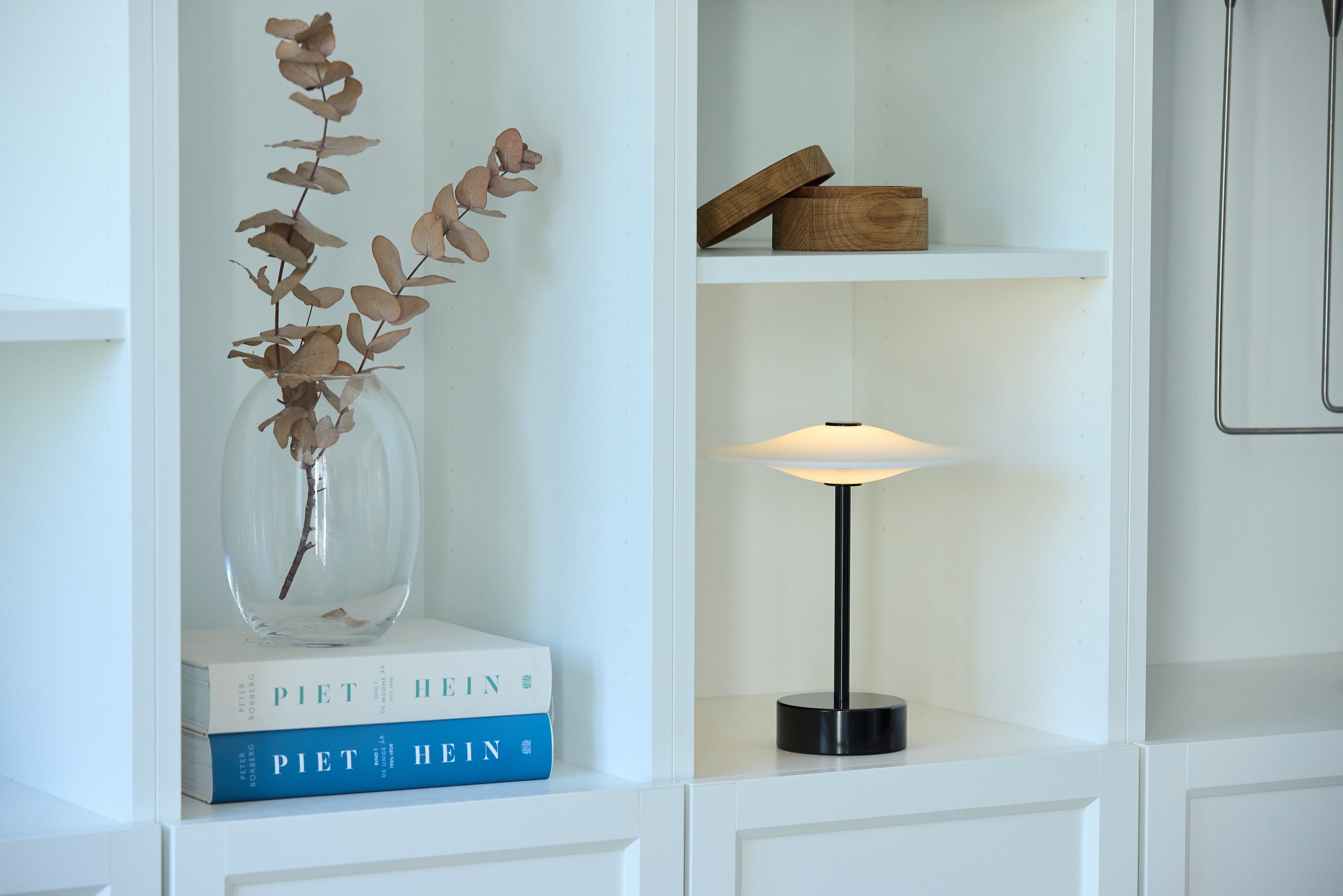 Den æstetiske Piet Hein Sinus22 Bordlampe i Sort placeret på hylden i stuen for dens behagelige belysning