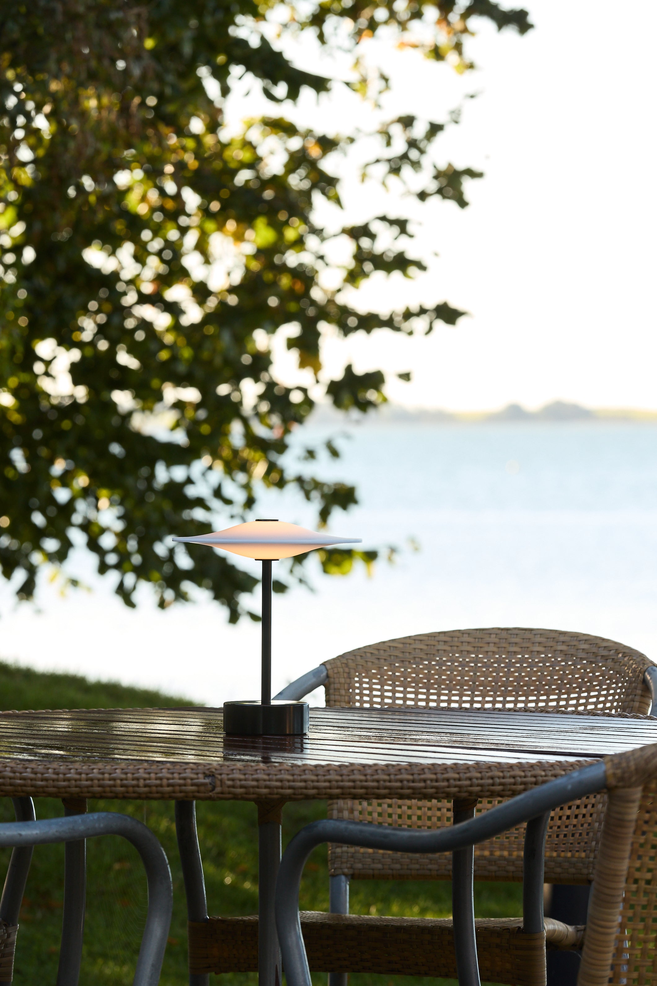 Piet Hein Sinus22 Bordlampe i Sort placeret udenfor på havebordet for dens varme belysning