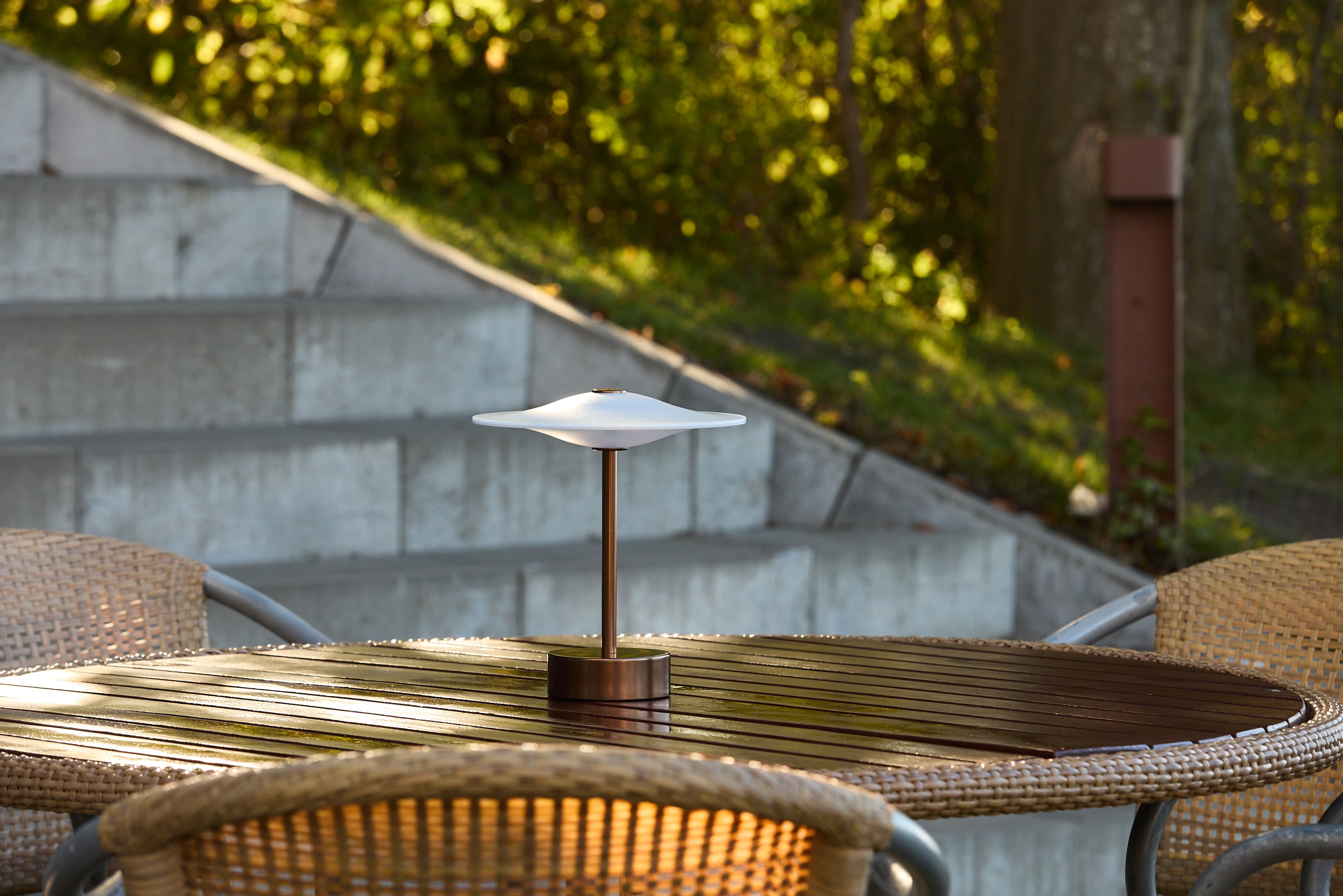 Piet Hein Sinus22 Bordlampe i Aged Bronze placeret udenfor på havebordet for dens varme belysning