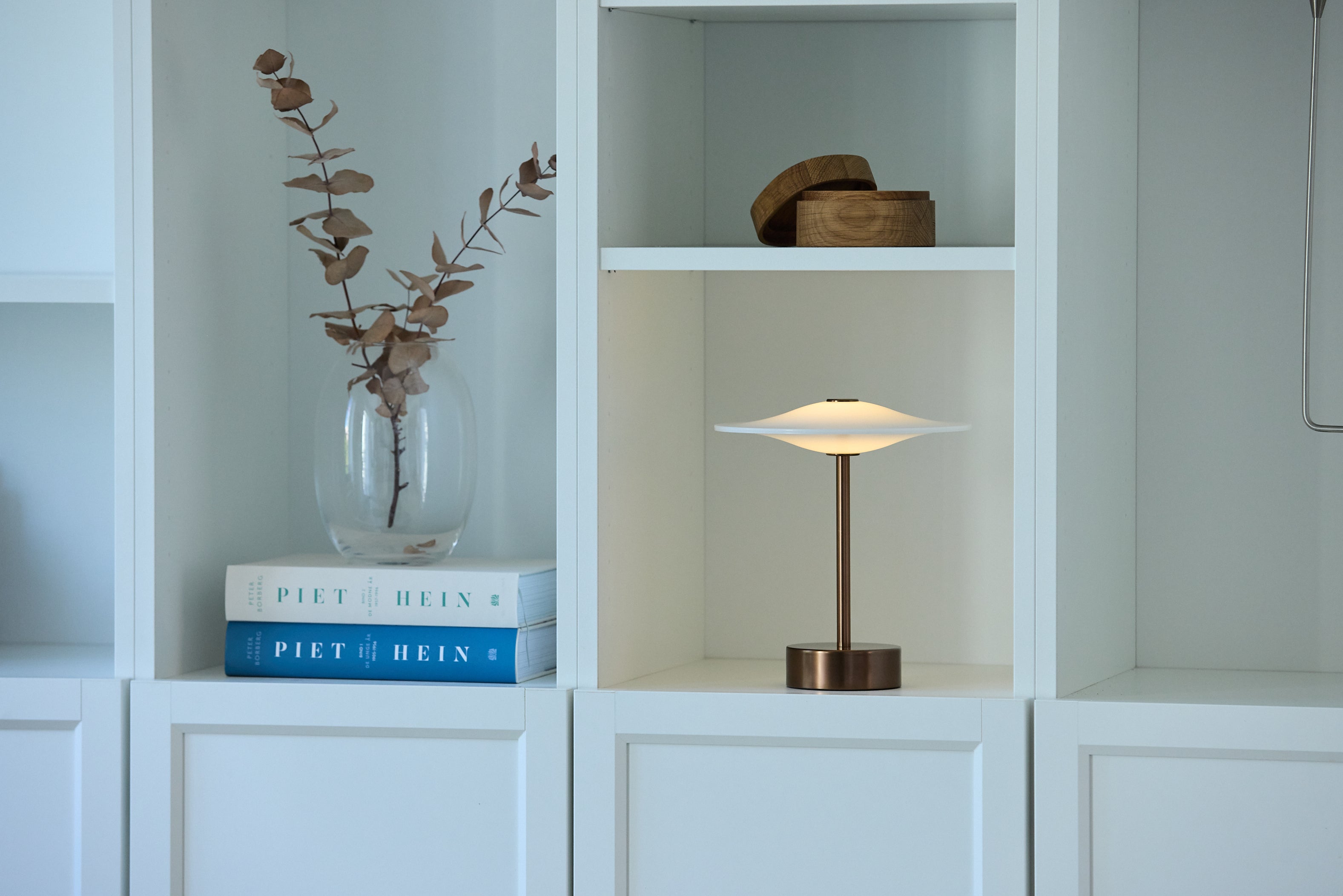 Den æstetiske Piet Hein Sinus22 Bordlampe i Aged Bronze placeret på en hylde i stuen for dens elegante design