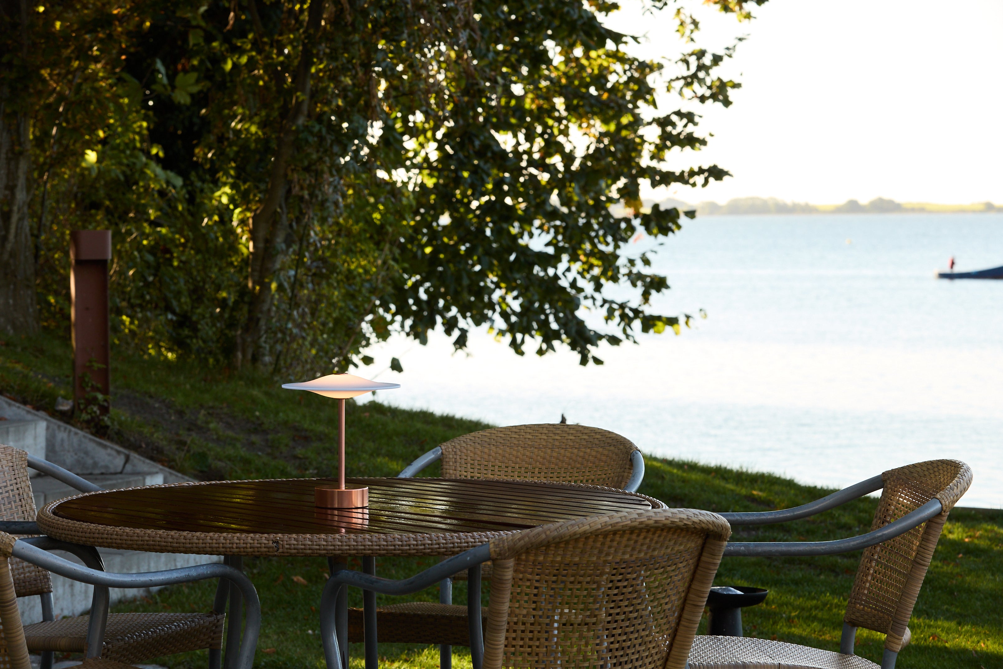 Piet Hein Sinus22 Bordlampe i Kobber placeret udenfor på havebordet for dens varme belysning og unikke design