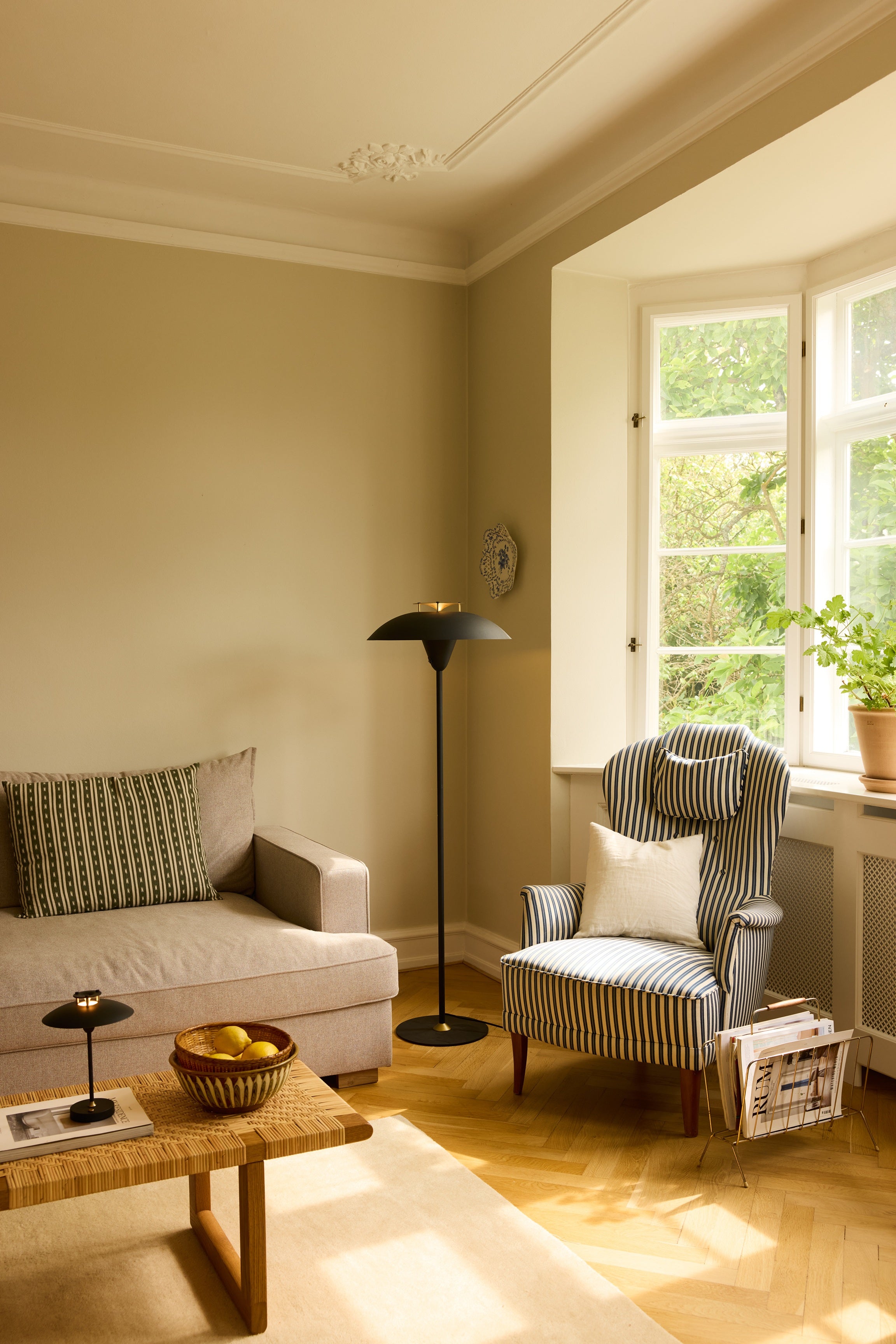 Den elegante designet Stepp Gulvlampe i Sort/Antique placeret i hjørnet af stuen for dens behagelige belysning