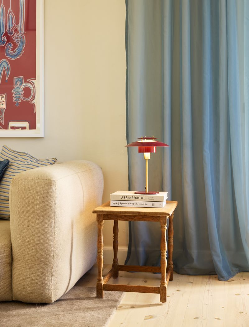 Sørup Bordlampe Ø25 Merlot placeret på et bord i stuen ved siden af sofaen for dens unikke design