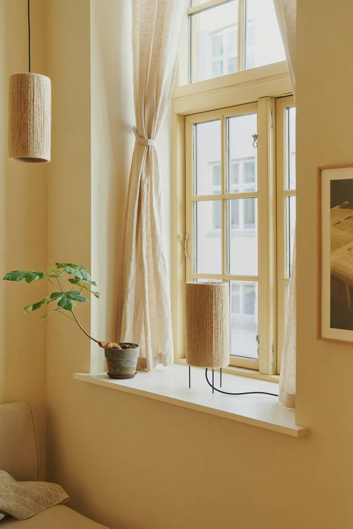 Den unikke og elegante designet Ro Ø15 Bordlampe i Jute placeret i vindueskammen for dens behagelige belysning