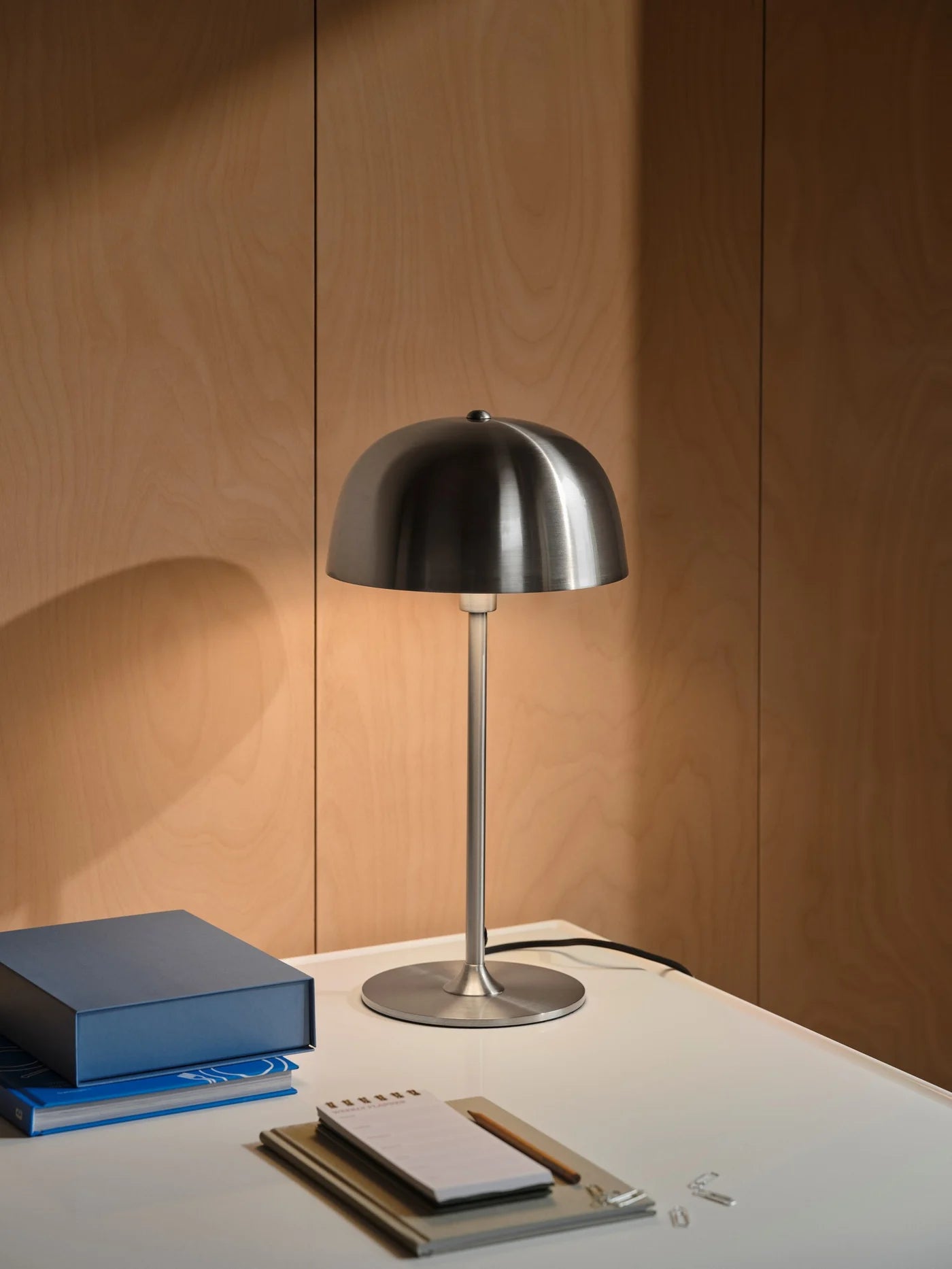 Den æstetiske Cera Bordlampe i Børstet Stål placeret på arbejdsbordet for dens varme belysning