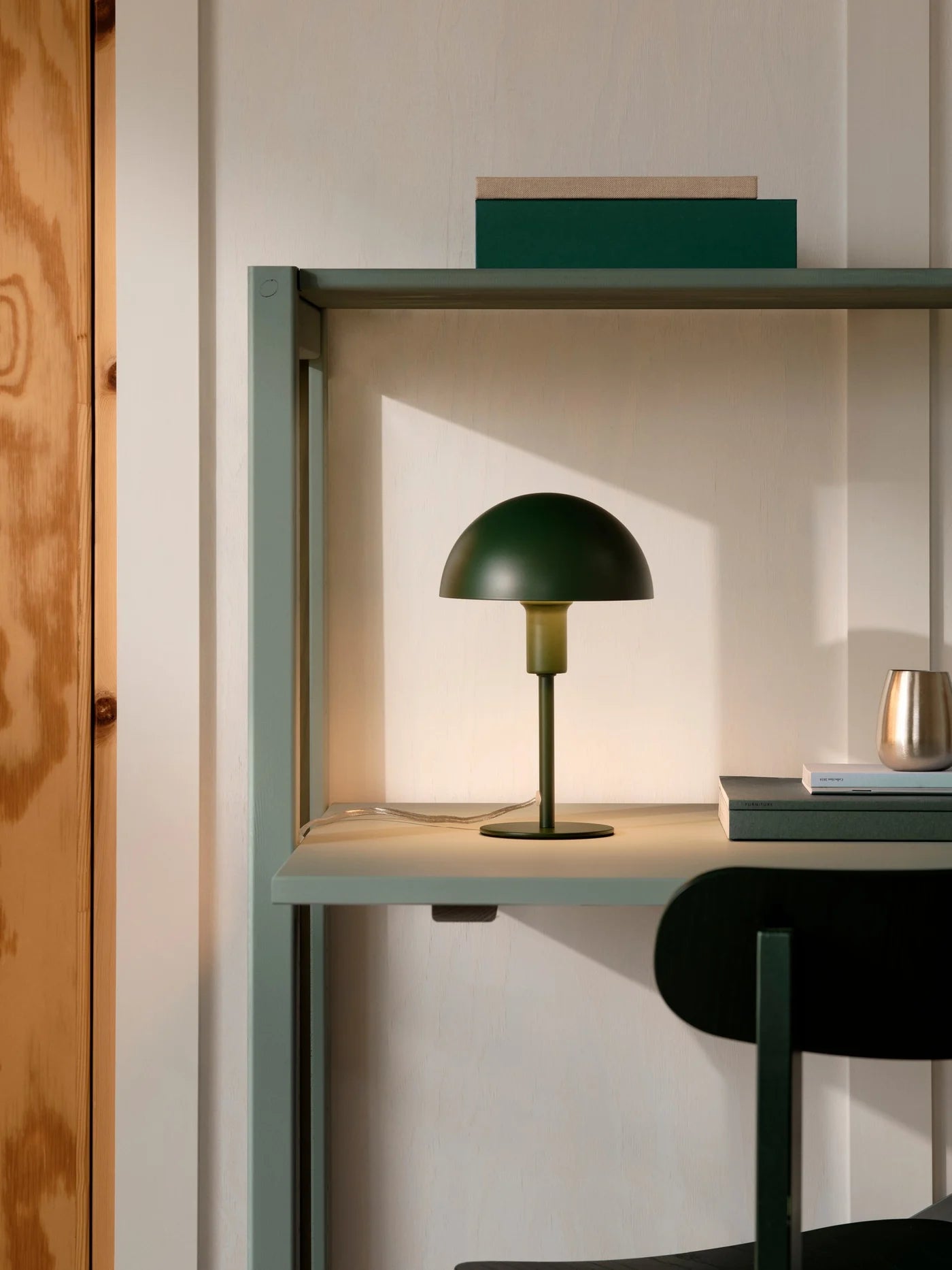 Den æstetiske Ellen Mini Bordlampe i Mørk Grøn placeret på arbejdsbordet for dens varme belysning