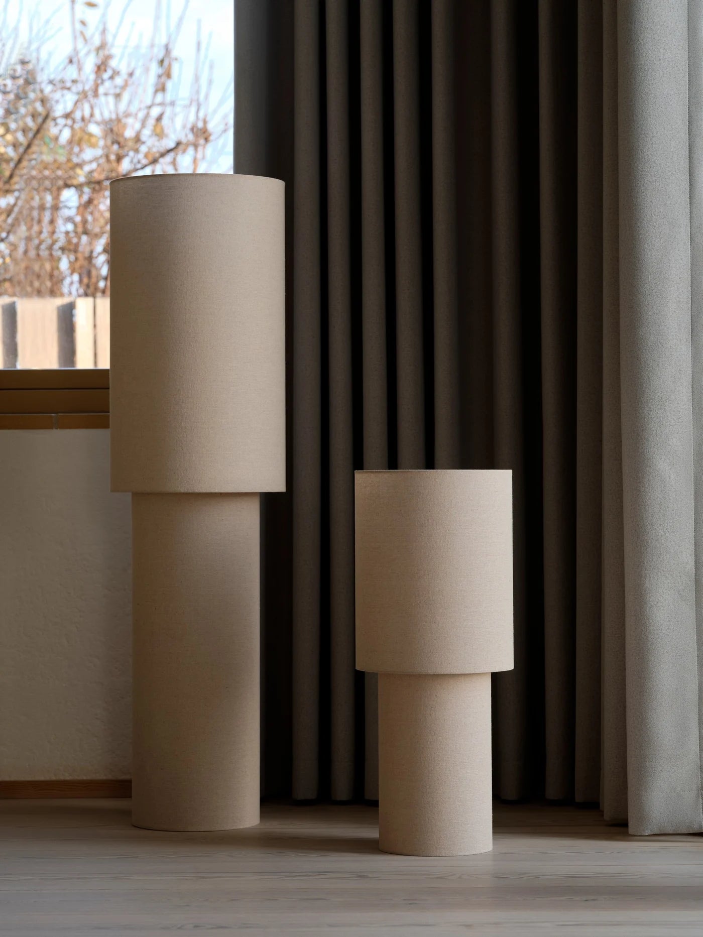 Den unikke designet Izara 60 Gulvlampe i Beige placeret i hjørnet af stuen med dens større variant