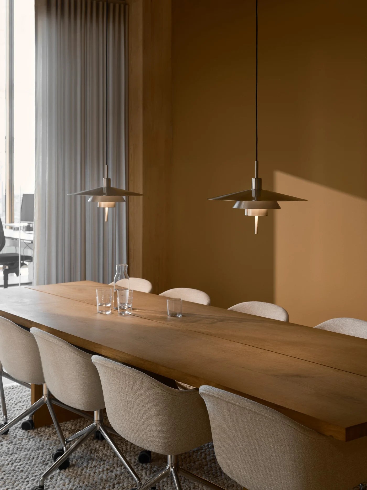 Den unikke og elegante designet Latika Pendel i Børstet Krom hængt op over mødebordet for dens varme belysning