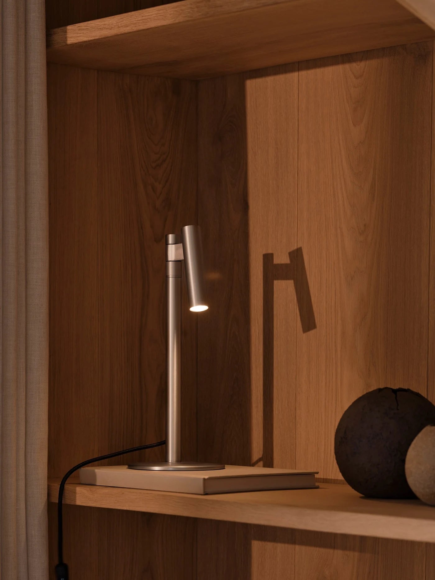 Den unikke designet Makoto Bordlampe i Satin Krom placeret på hylden for dens behagelige belysning