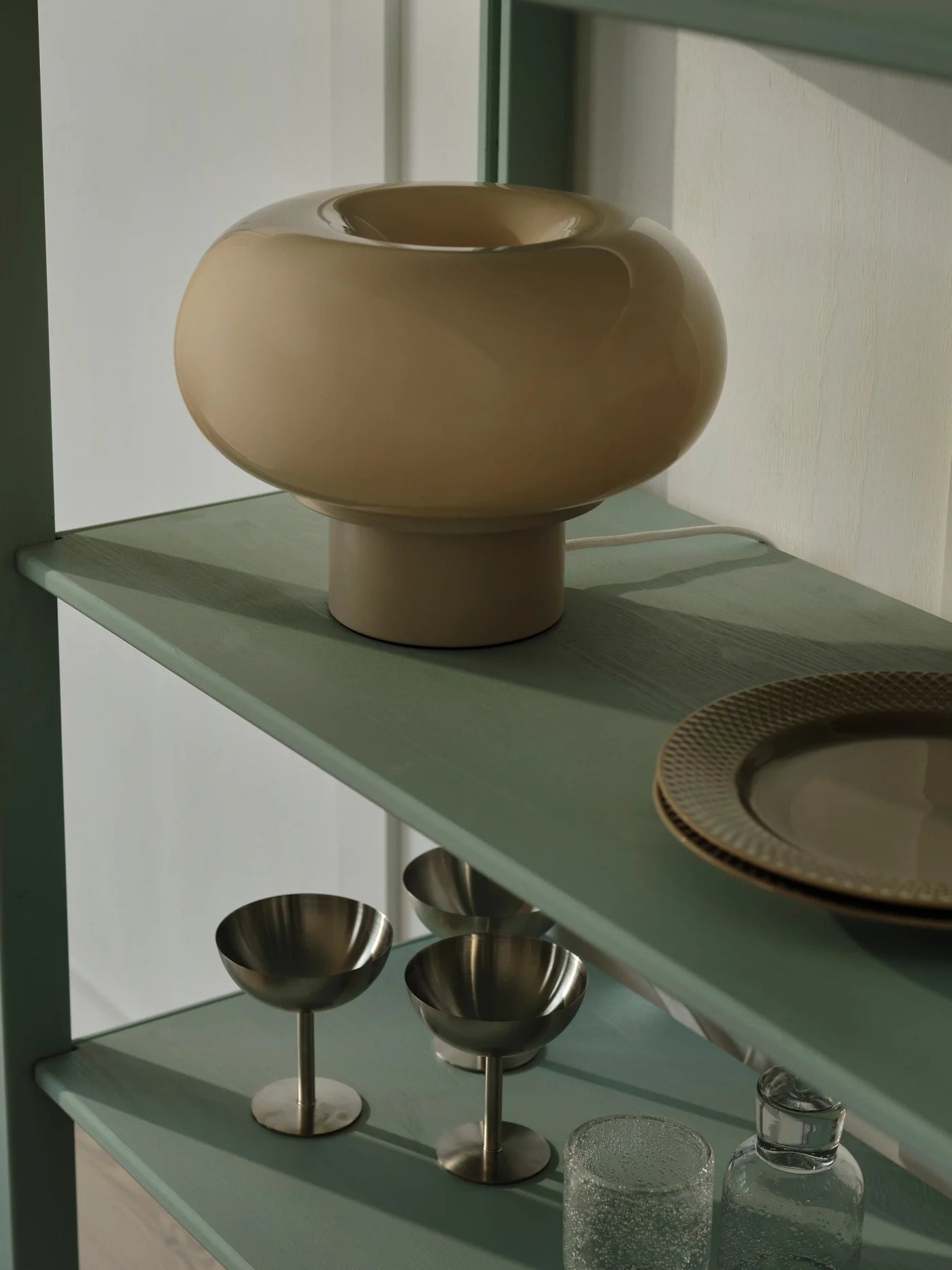 Den elegante Malti Bordlampe i Beige placeret på hylden i stuen for dens unikke design