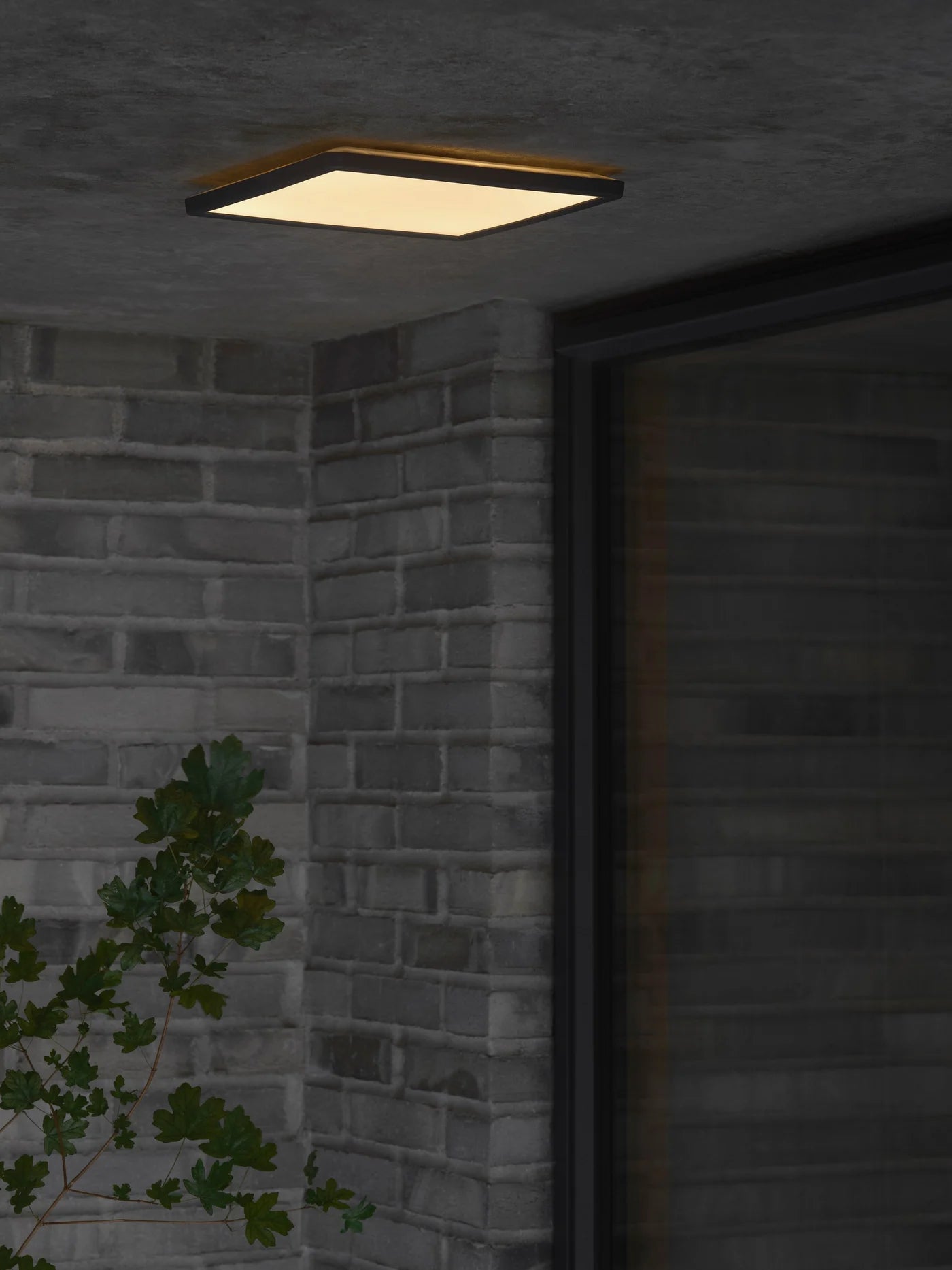 Den elegante Oja Ø29 Outdoor Square Loftlampe i Sort hængt op udenfor under halvtaget for dens unikke belysning