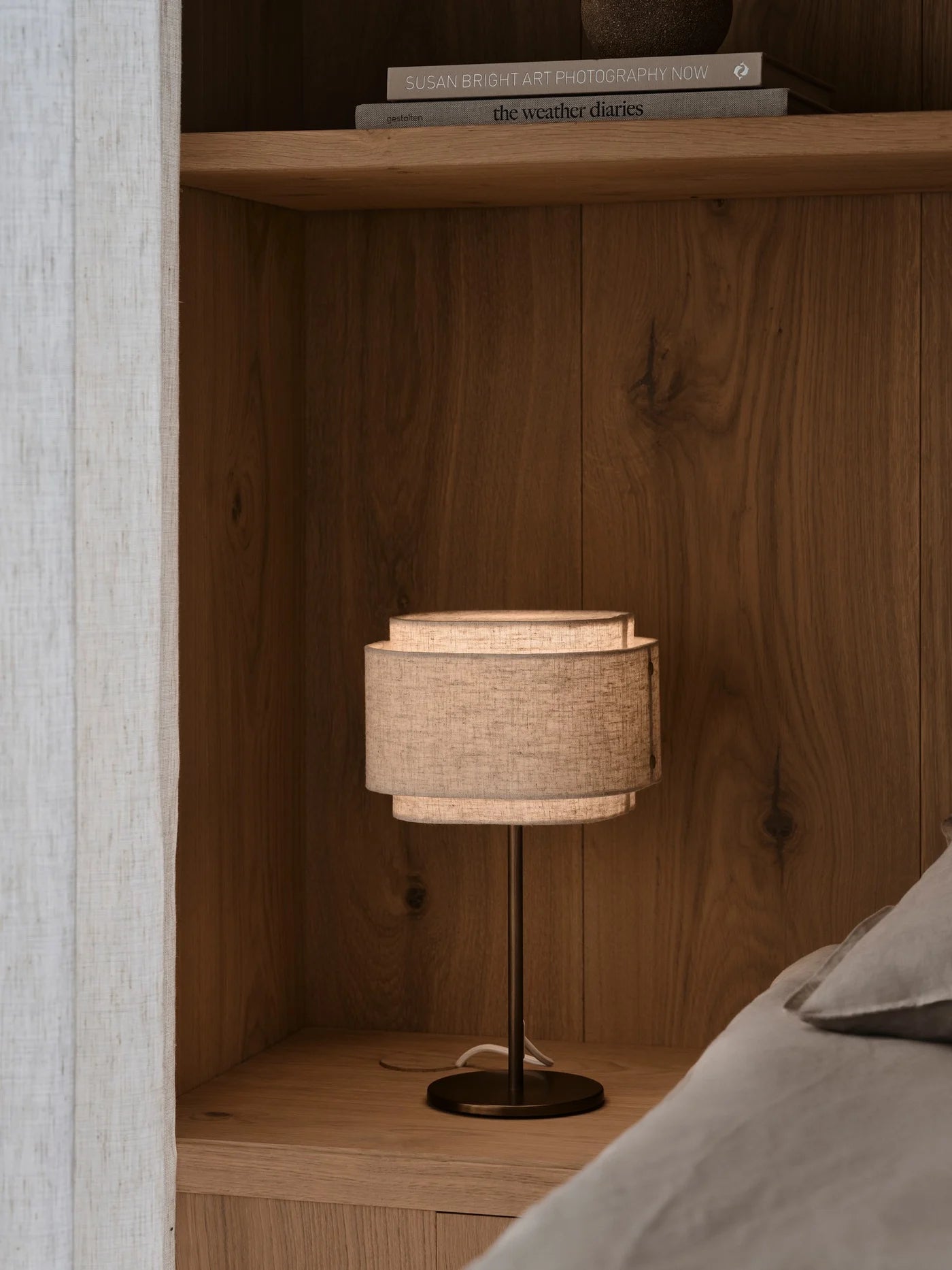 Den unikke designet Takai Bordlampe i Beige placeret på hylden for dens varme belysning