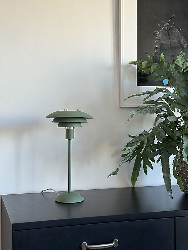 Den æstetiske Epsilon Bordlampe i Grøn placeret i stuen for dens elegante design og flotte kontrast