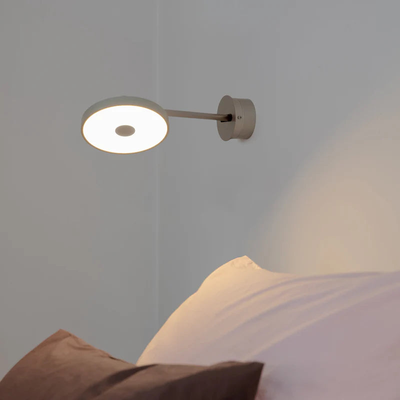 Den æstetiske Asteria Væglampe Long Hardwired i Nuance Mist/Stål hængt op ved siden af sengen for dens behagelige belysning