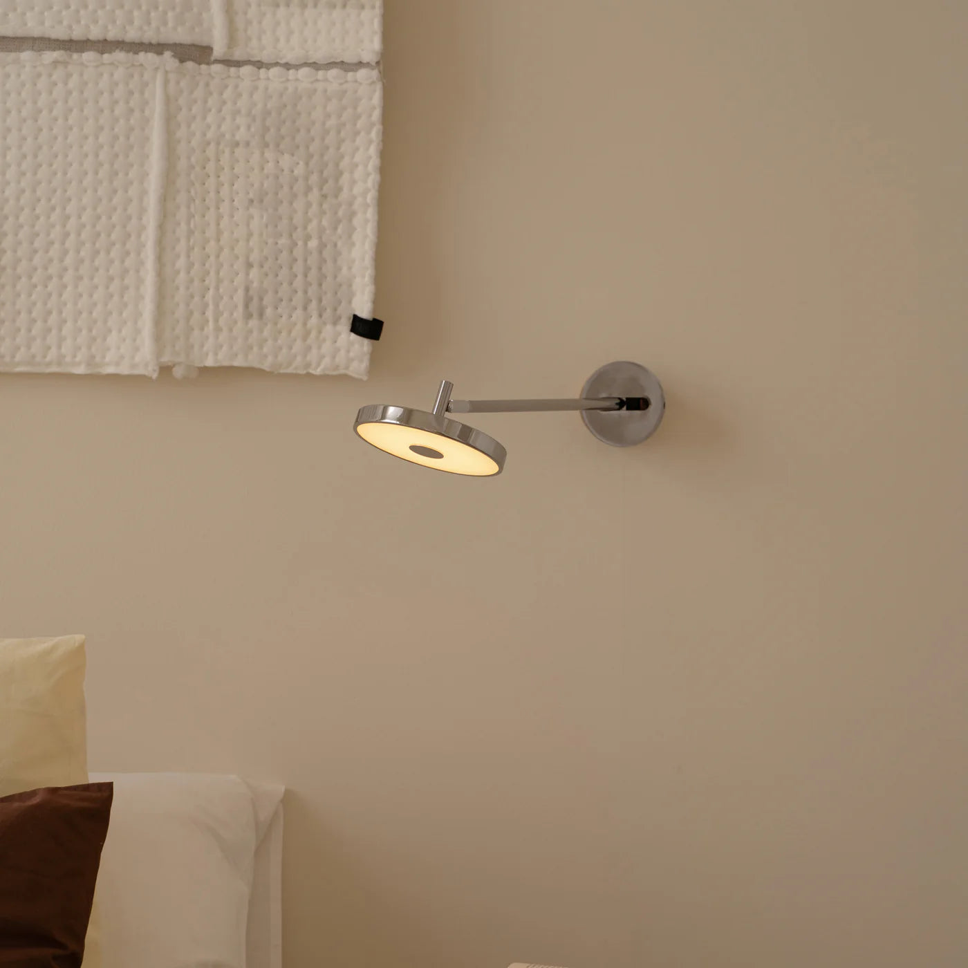 Zoomet ind på den unikke designet Asteria Væglampe Long Monochrome Hardwired i Polished Stål hængt op på væggen ved sengen