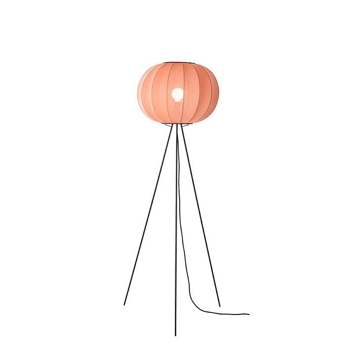 Den æstetiske Knit-Wit Ø45 Round Gulvlampe High i Coral placeret foran en væg med en tændt E27 pære