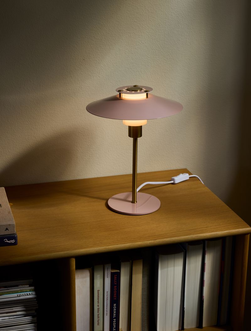 Rivoli Bordlampe Ø24 Rose placeret på en hylde for dens varme belysning