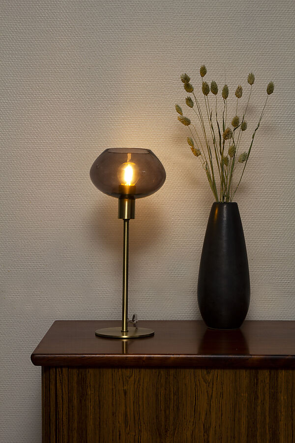 Den æstetiske Bell Bordlampe i Messing/Røg placeret på hylden i stuen for dens varme belysning